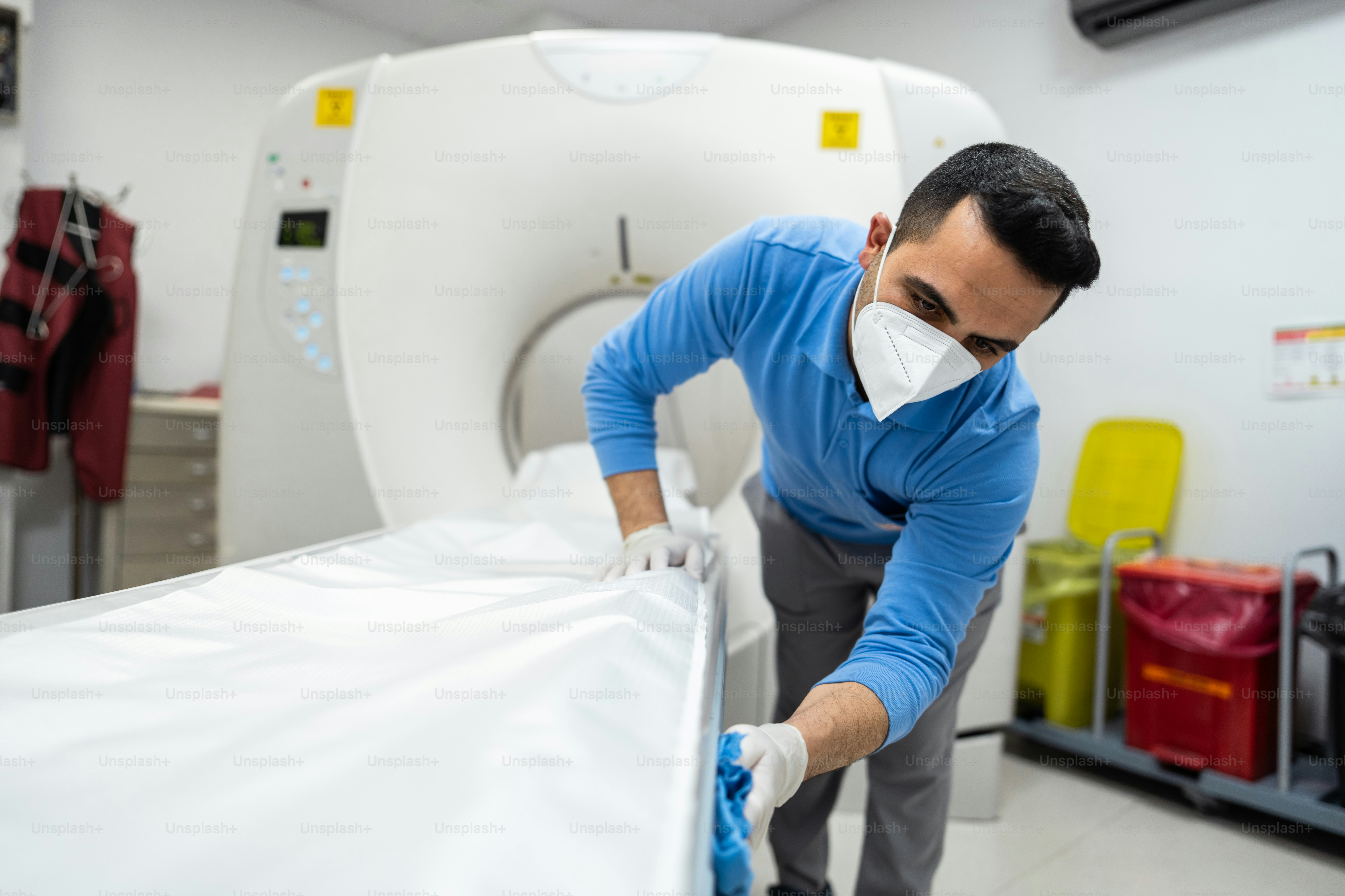 Man in mask cleans medical scanner bed
