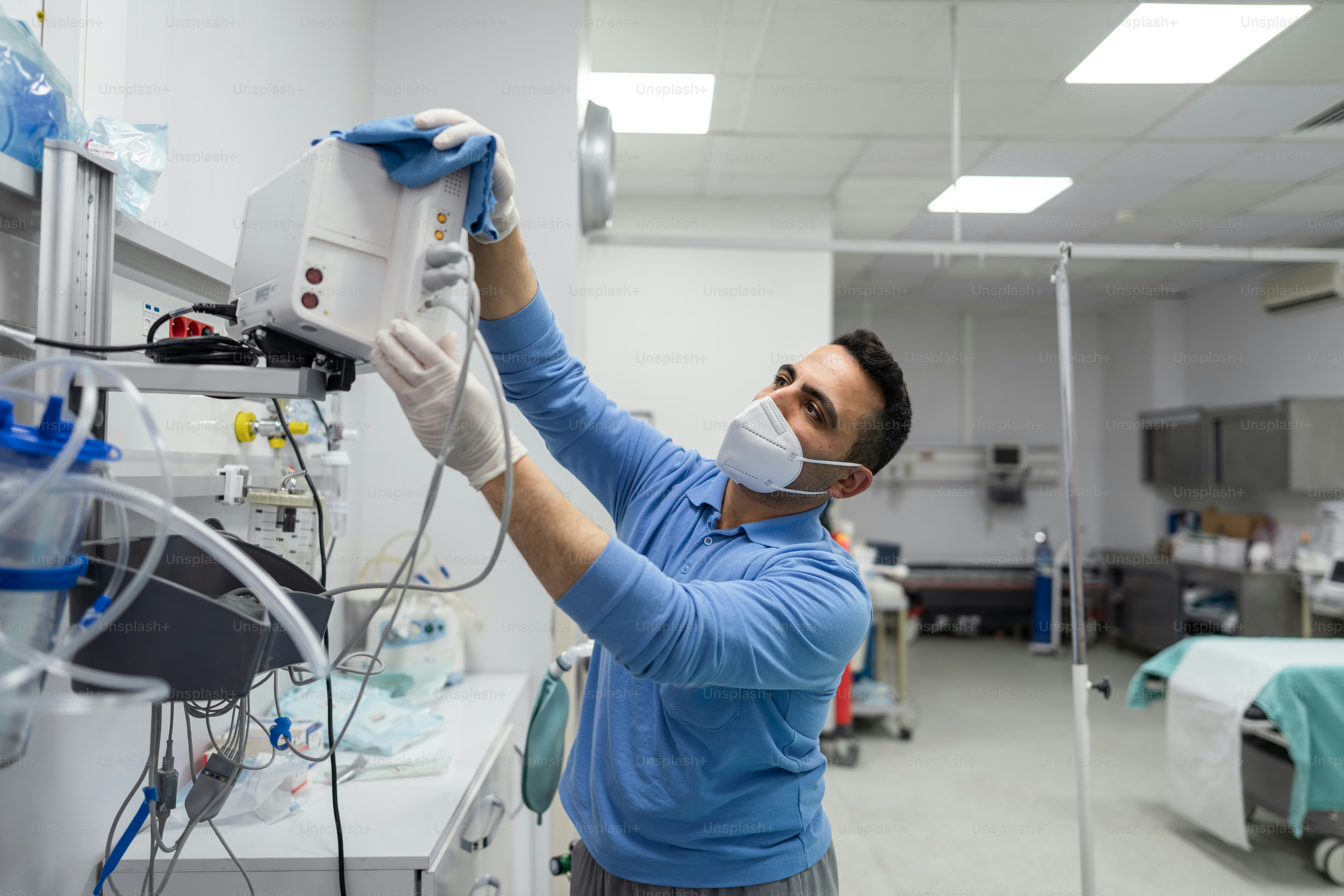 Man in mask cleans medical equipment with cloth.