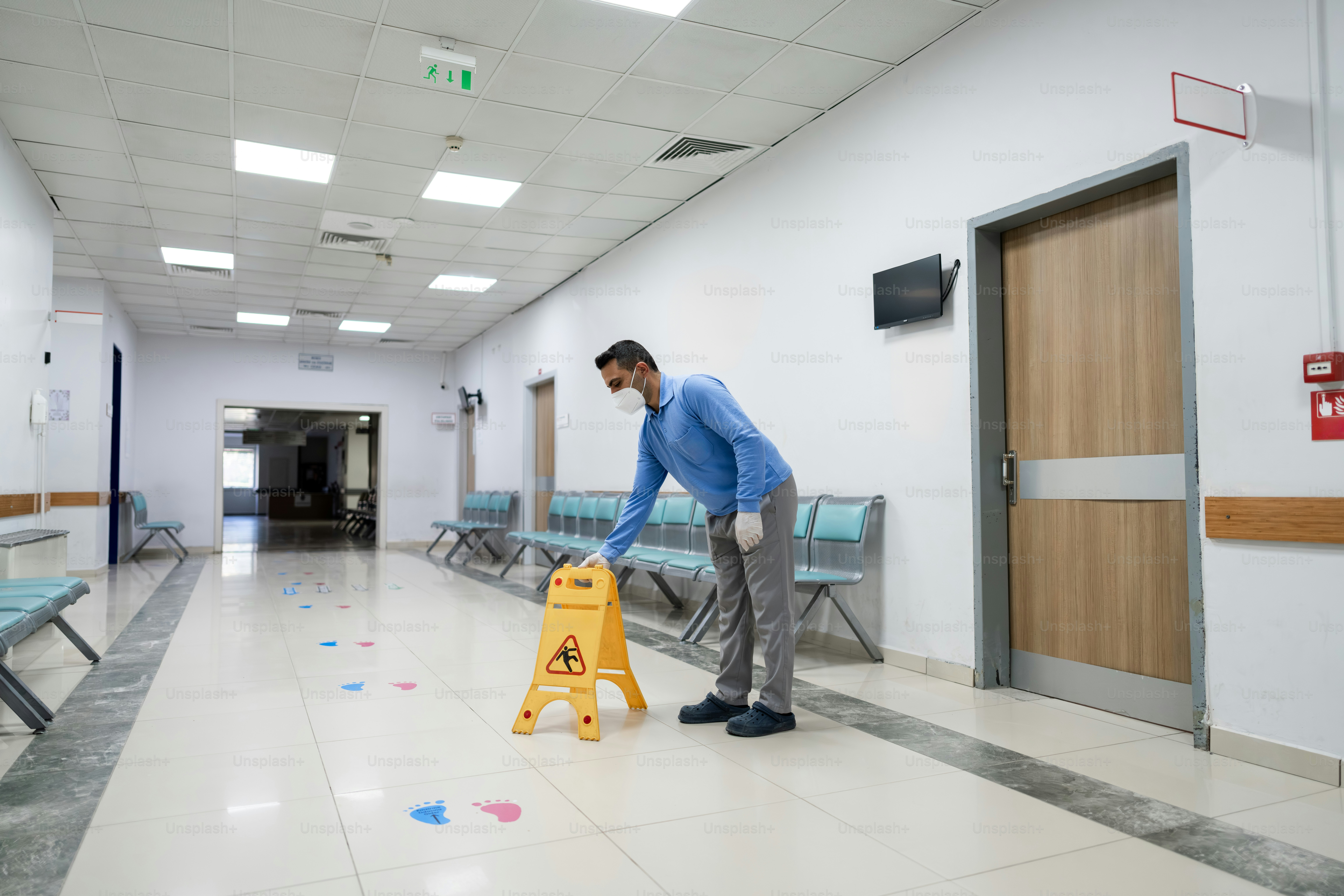Man in mask places wet floor sign in hallway.