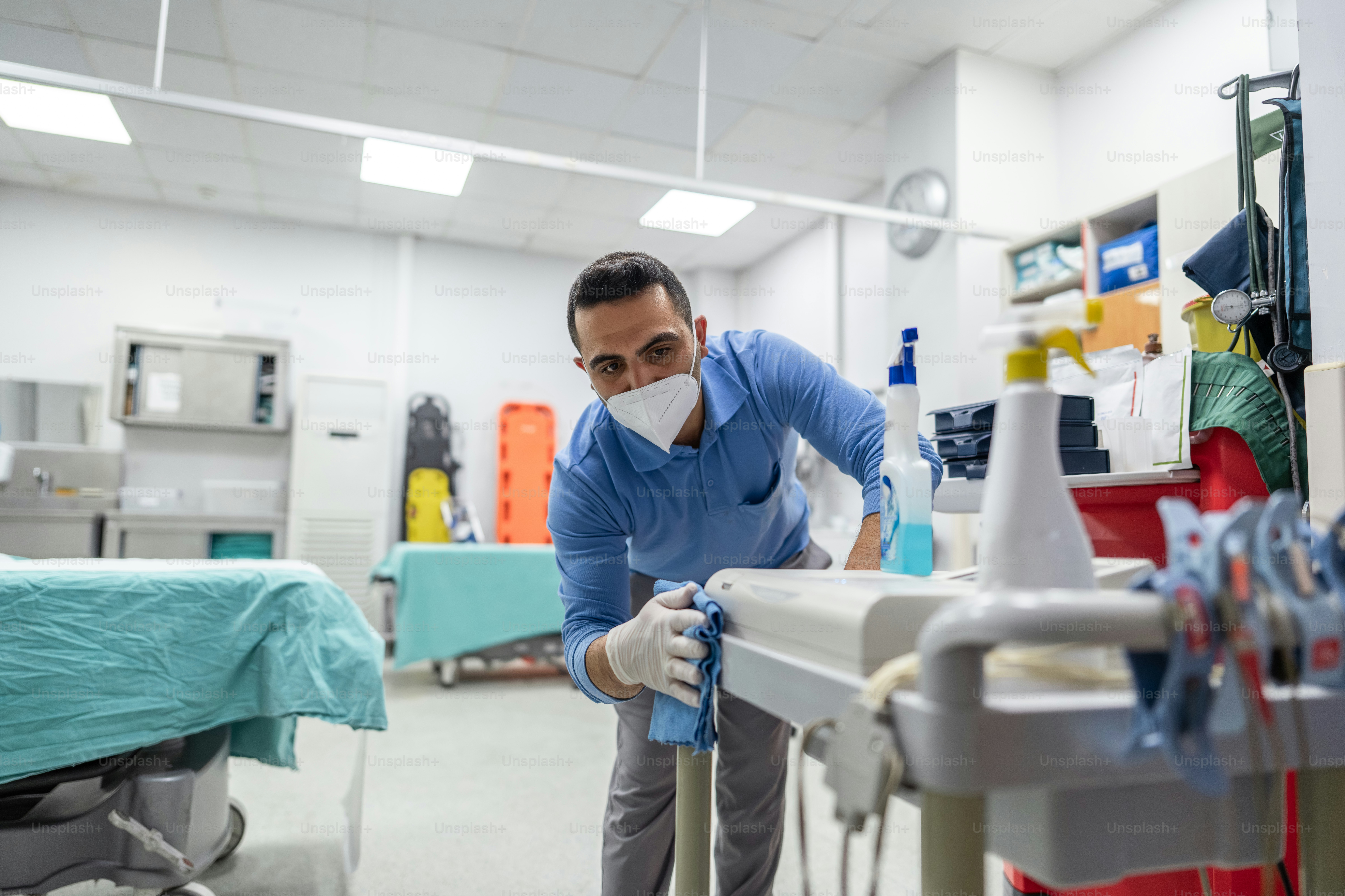 Man in mask cleans medical equipment with spray bottle.