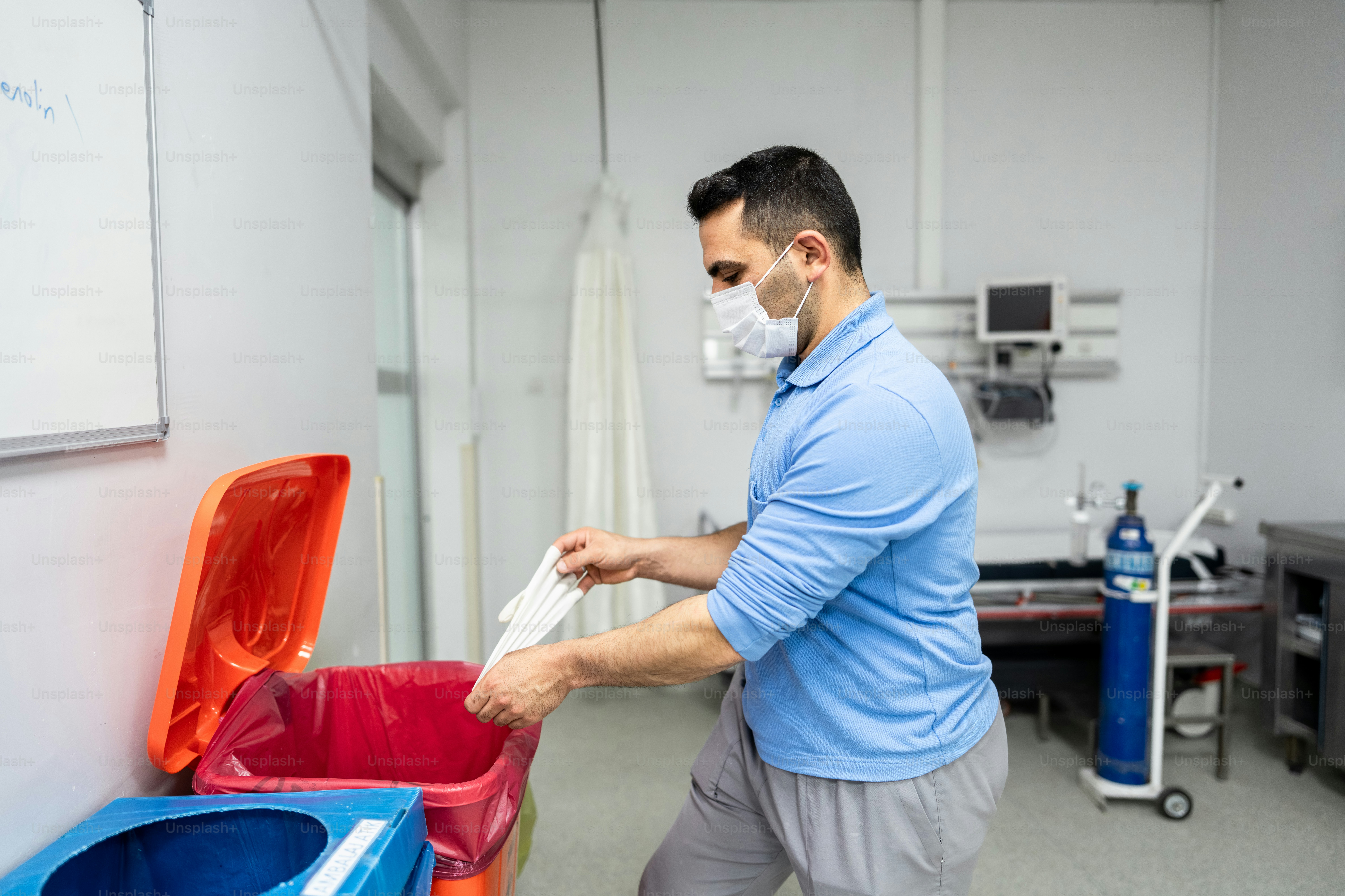 Man in mask discards medical gloves in bin.