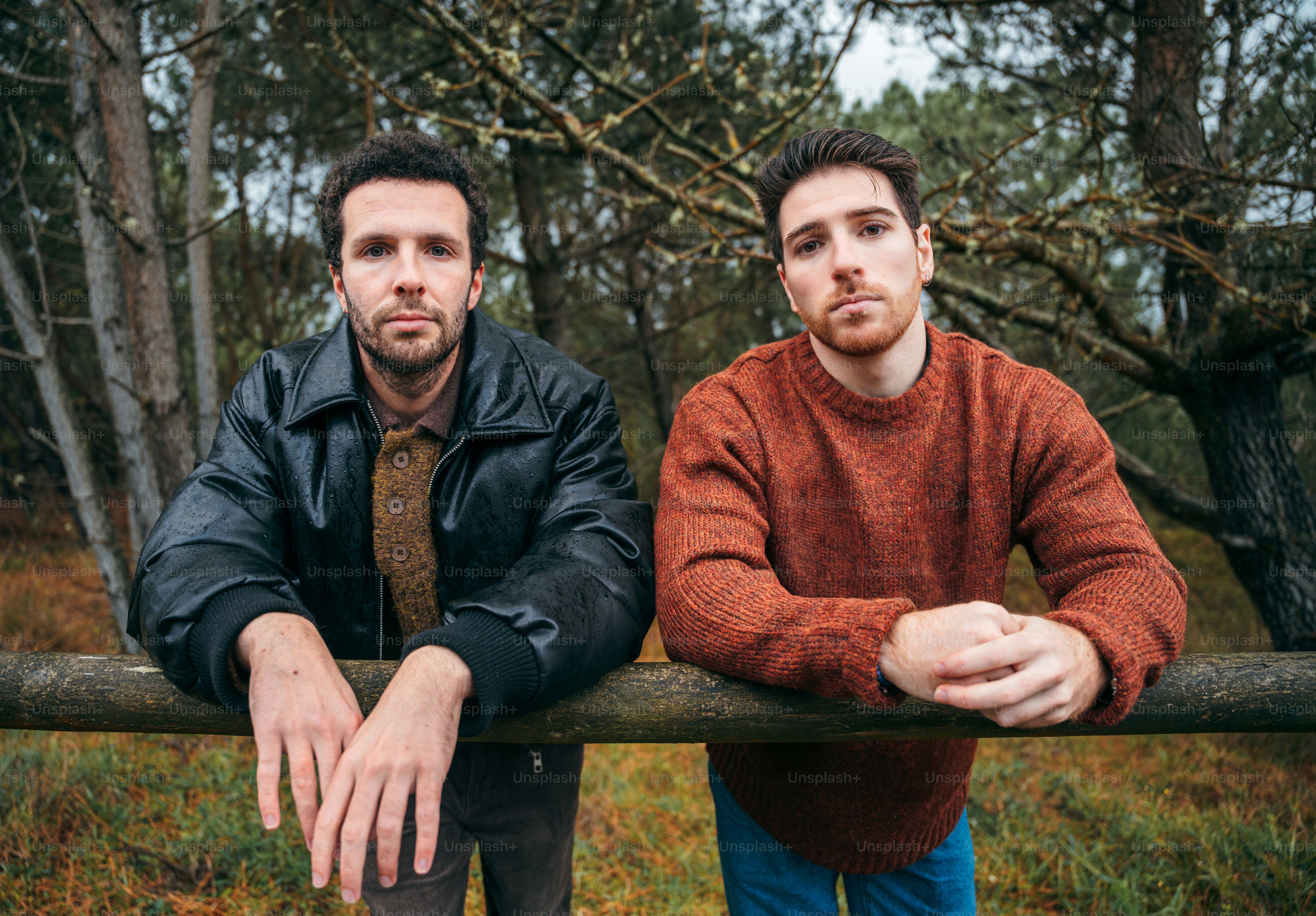 Two men leaning on a wooden fence outdoors.