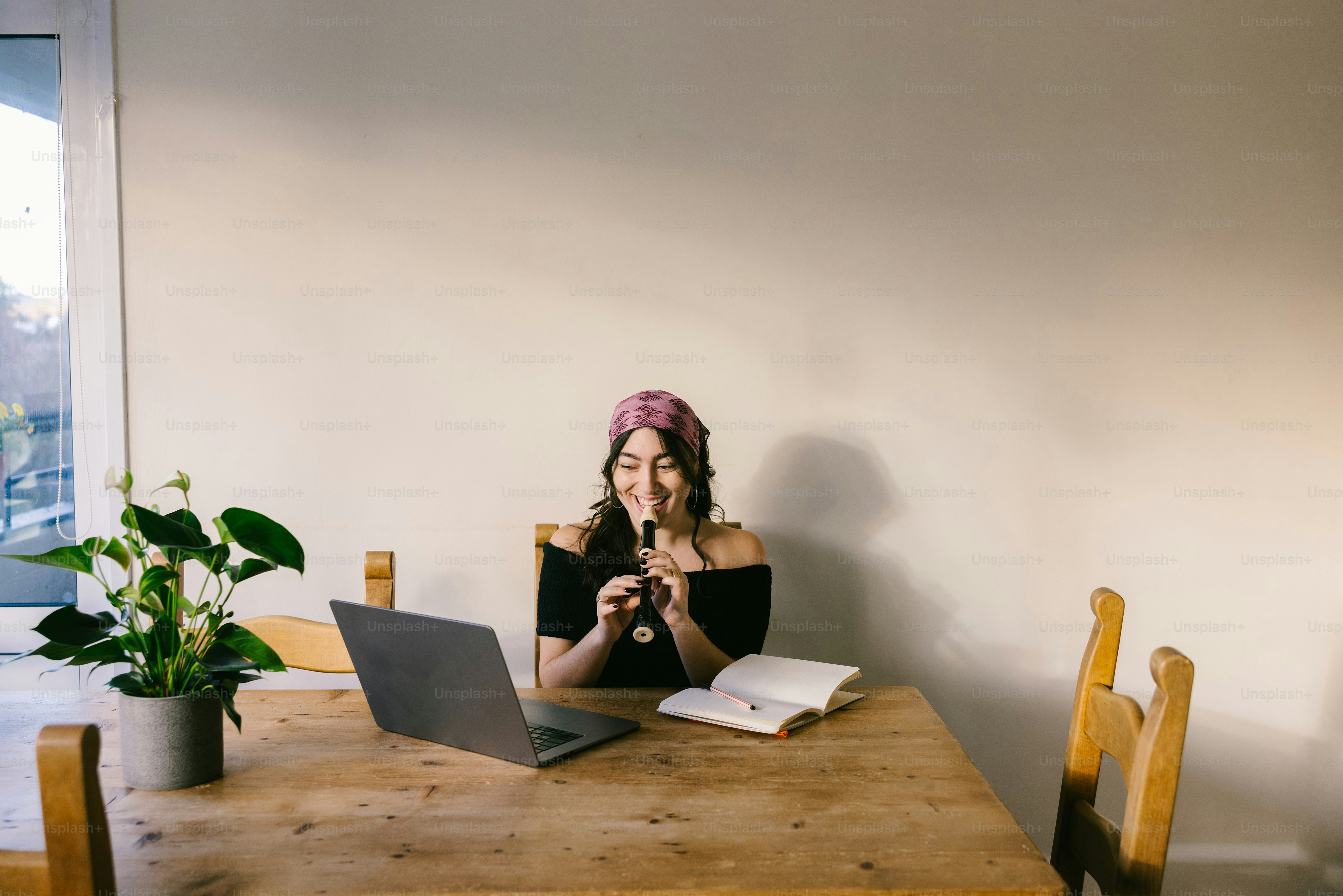 Woman playing flute at table with laptop and book.