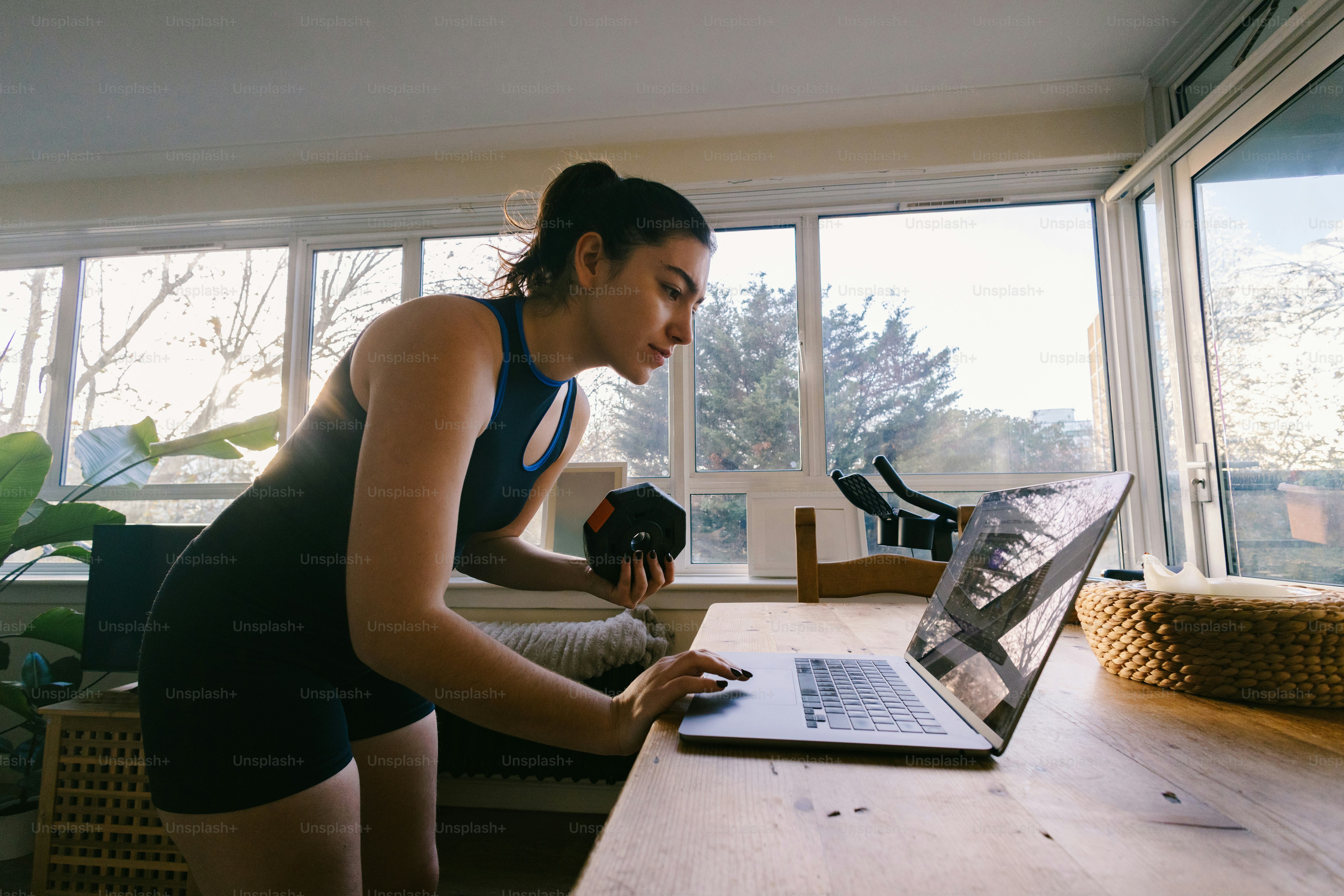 Woman exercising with dumbbell and laptop at home.