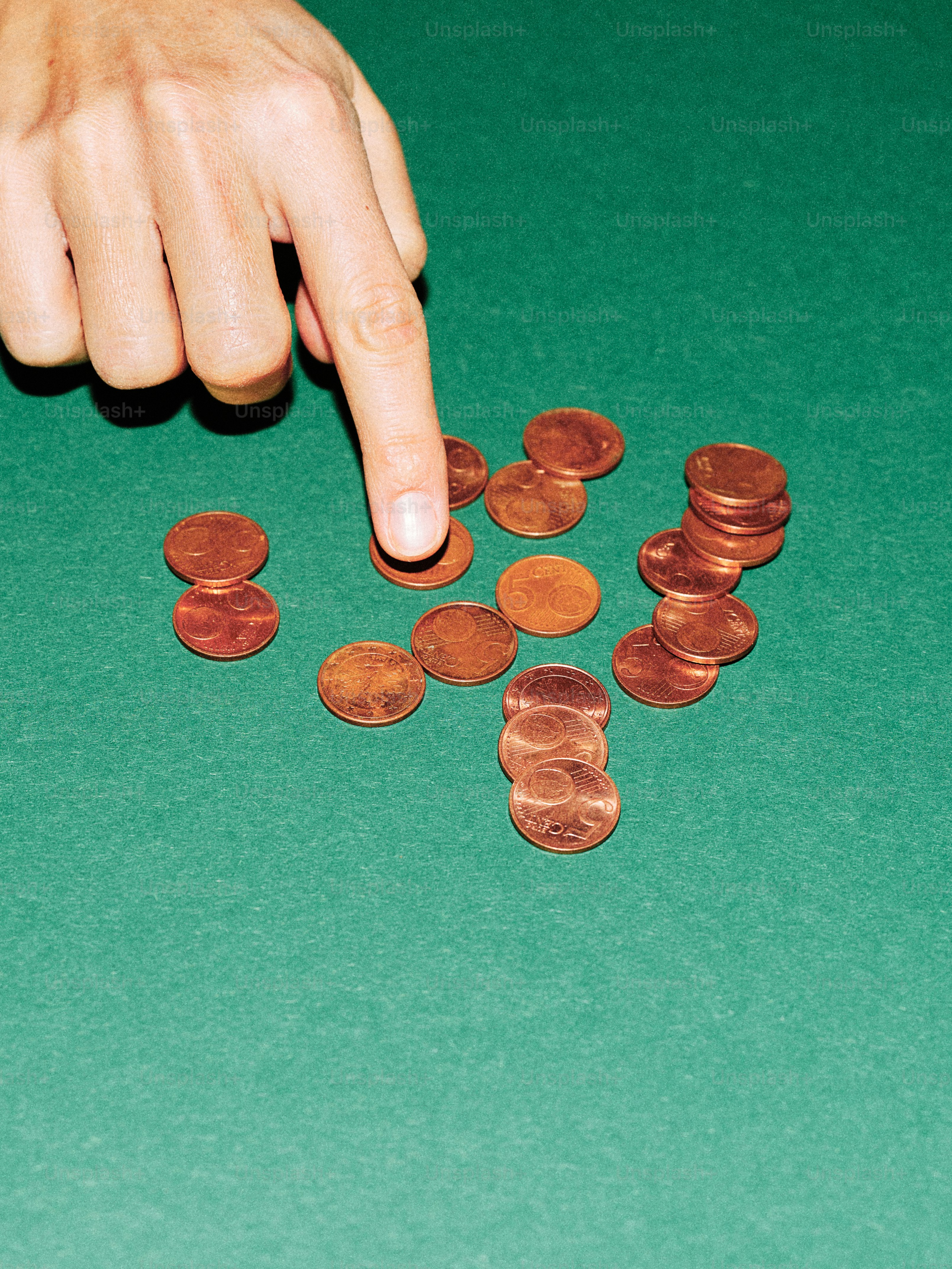 Finger pointing at scattered copper coins on green felt.