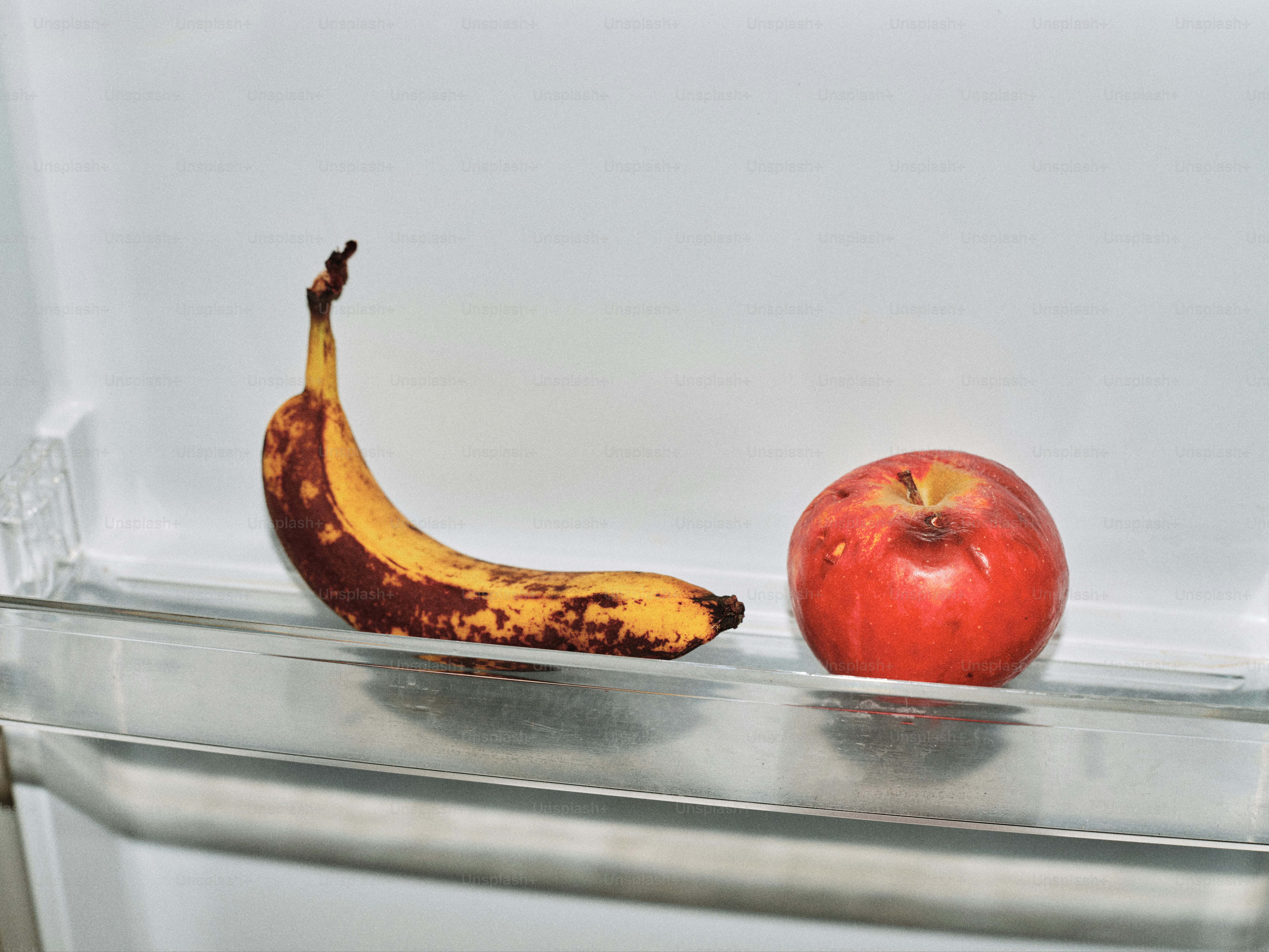 A bruised banana and a red apple on a shelf.
