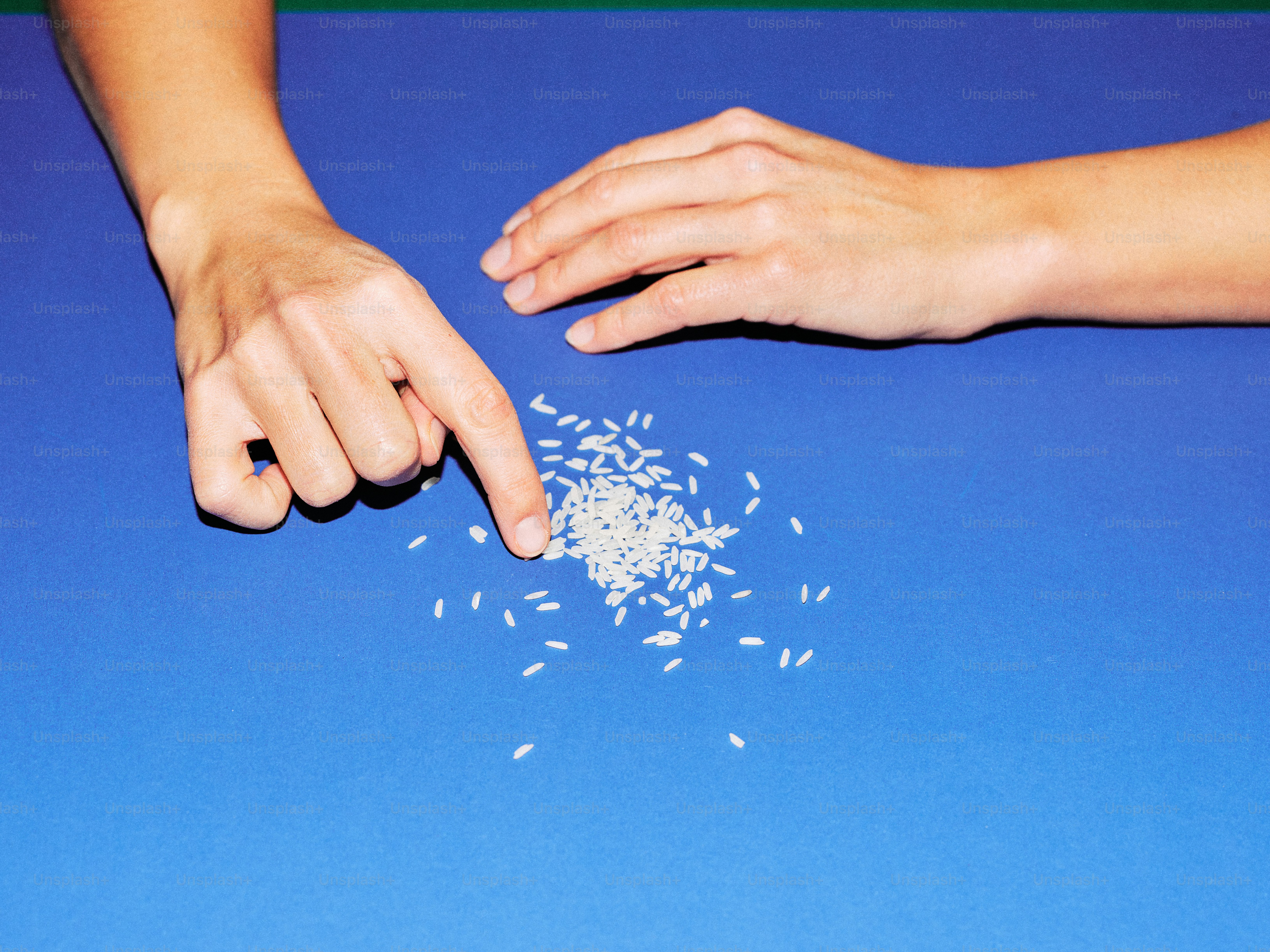 Hands pointing at a pile of rice grains.