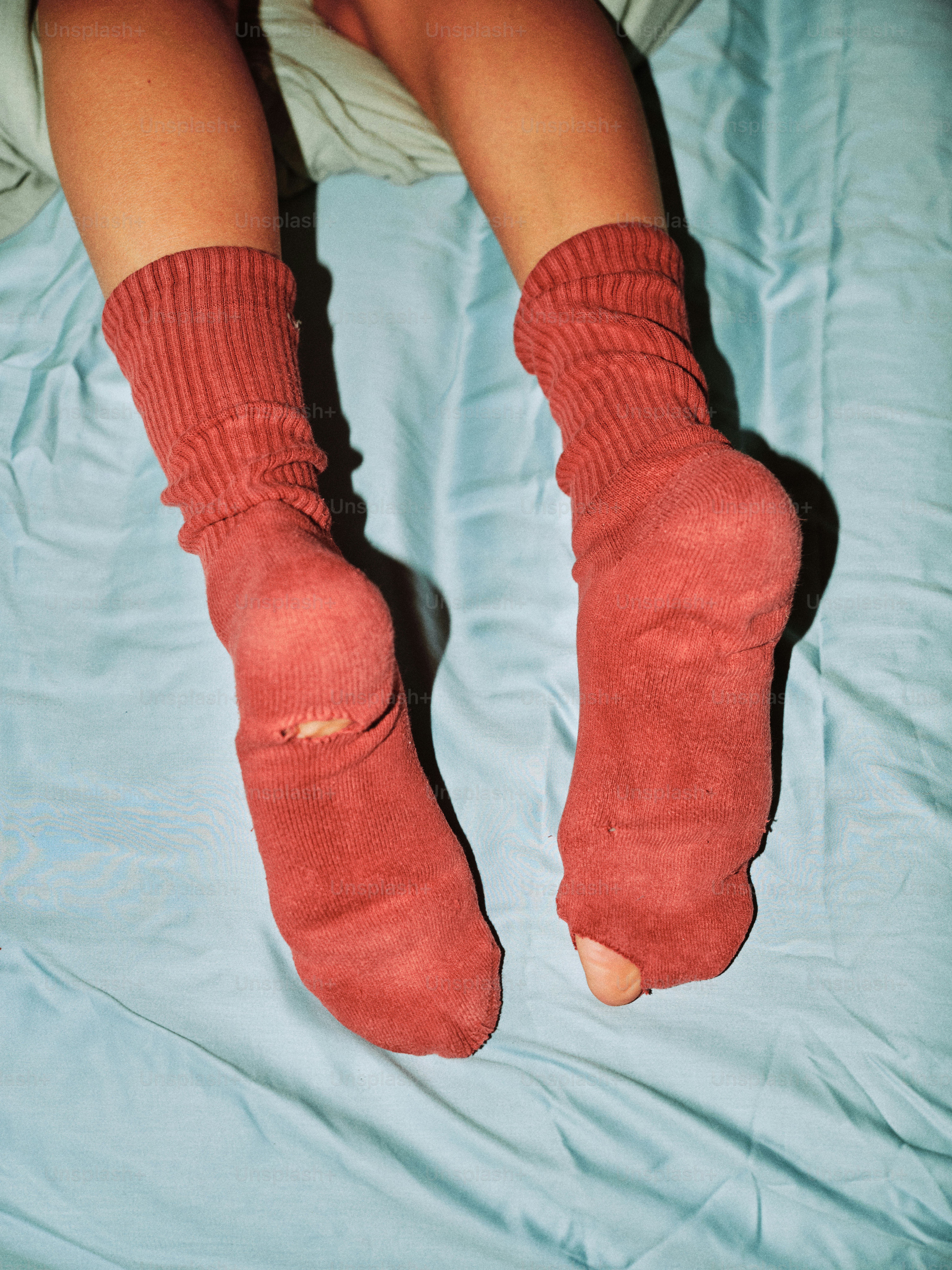 Pair of worn, red socks with holes on blue sheets