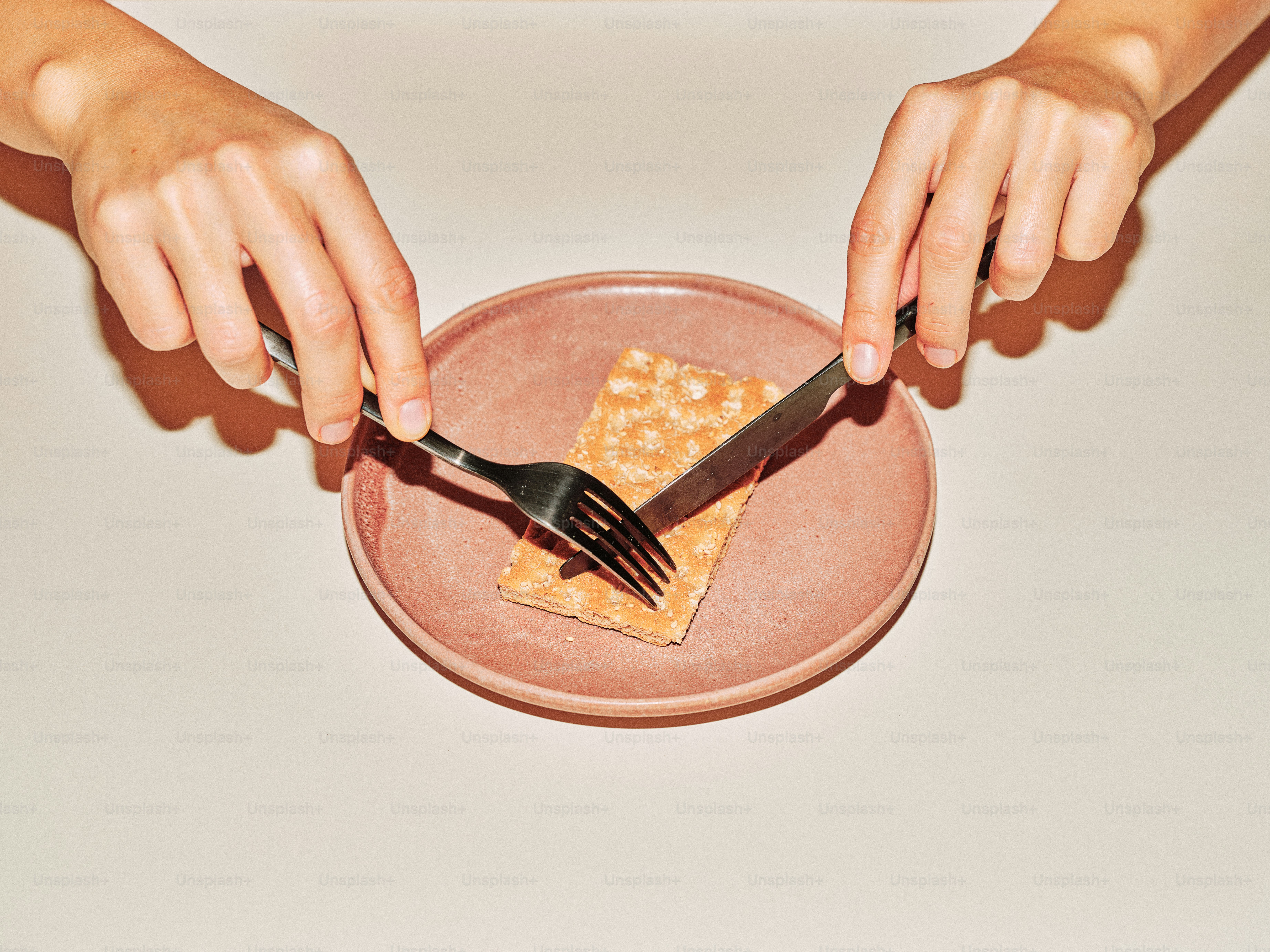 Hands cutting a cracker on a pink plate