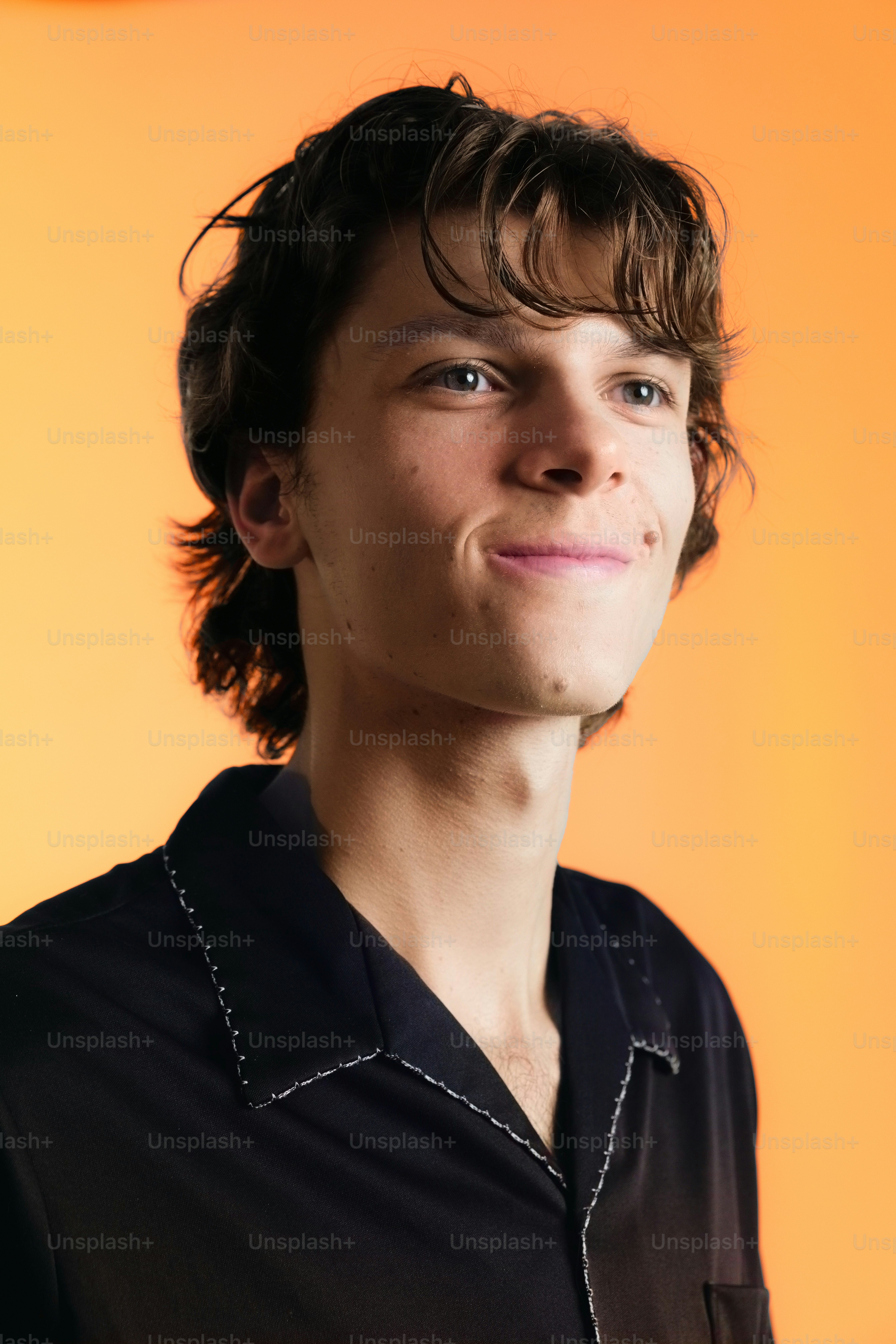 Jovem de cabelo castanho sorrindo contra fundo laranja