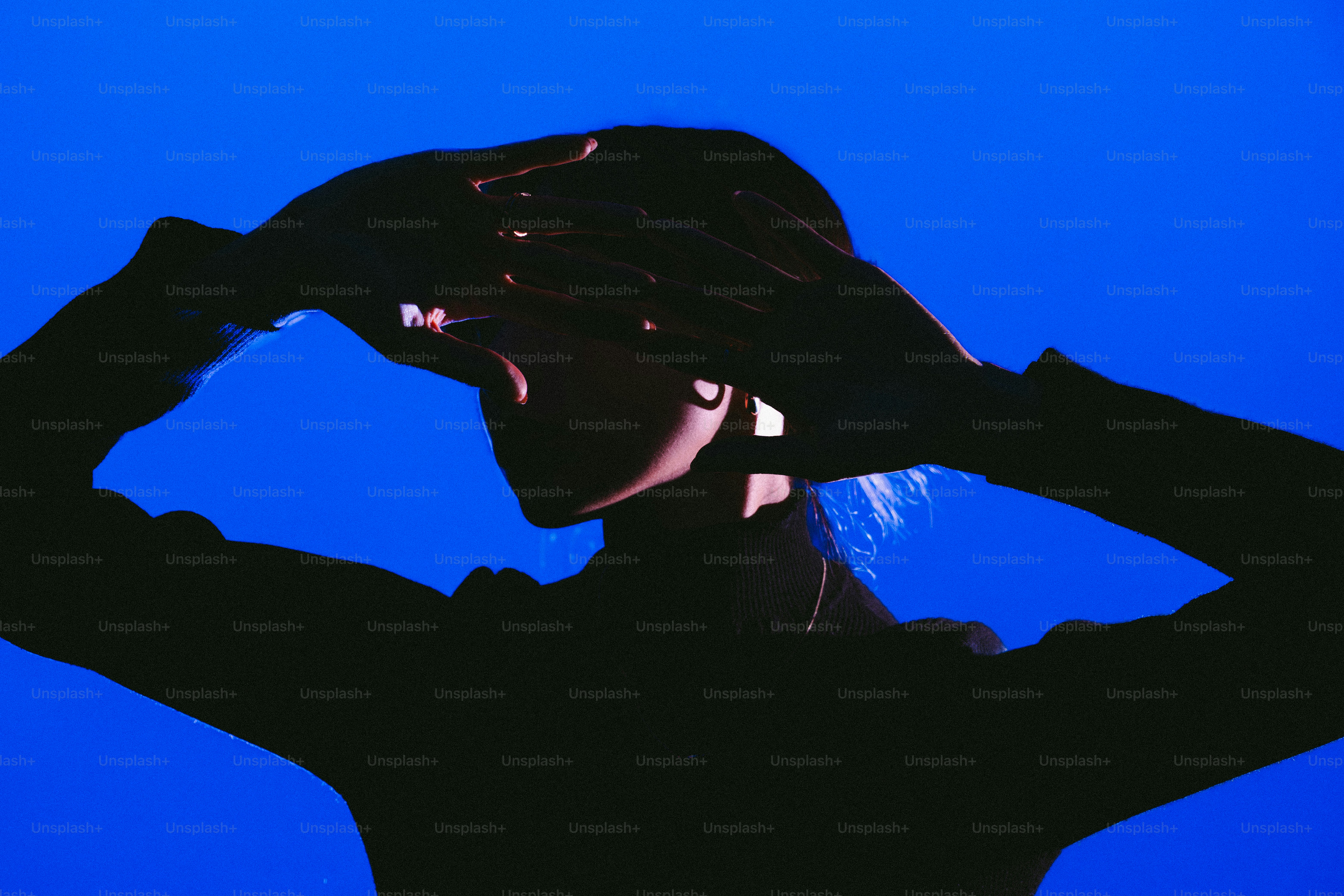 Silhouette of a person shielding eyes against blue background
