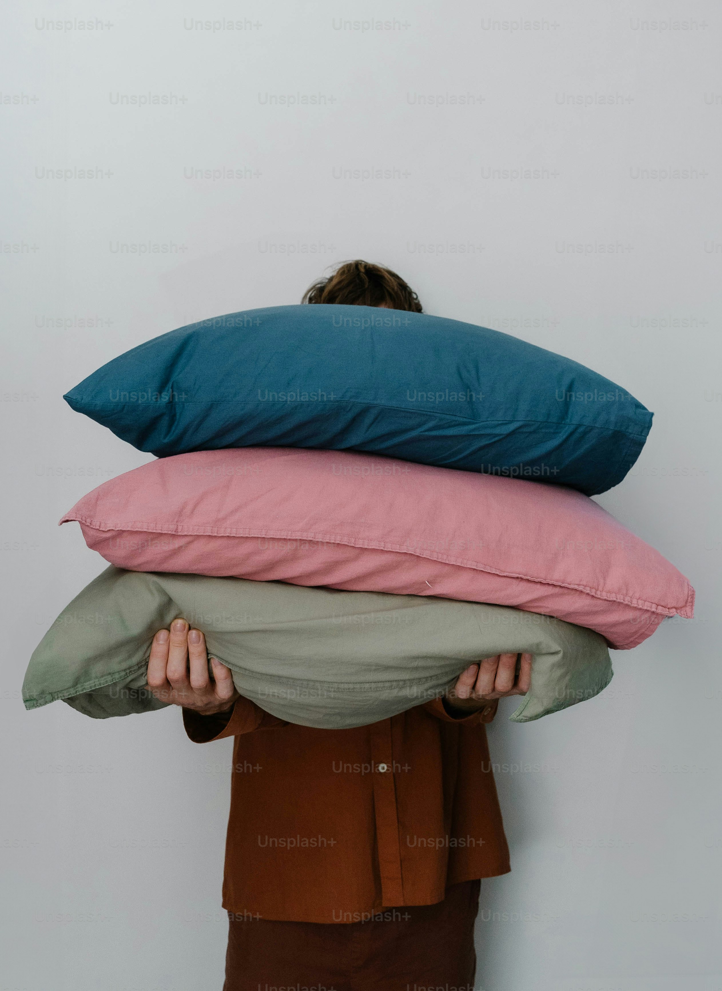 Person holding a stack of three colorful pillows.