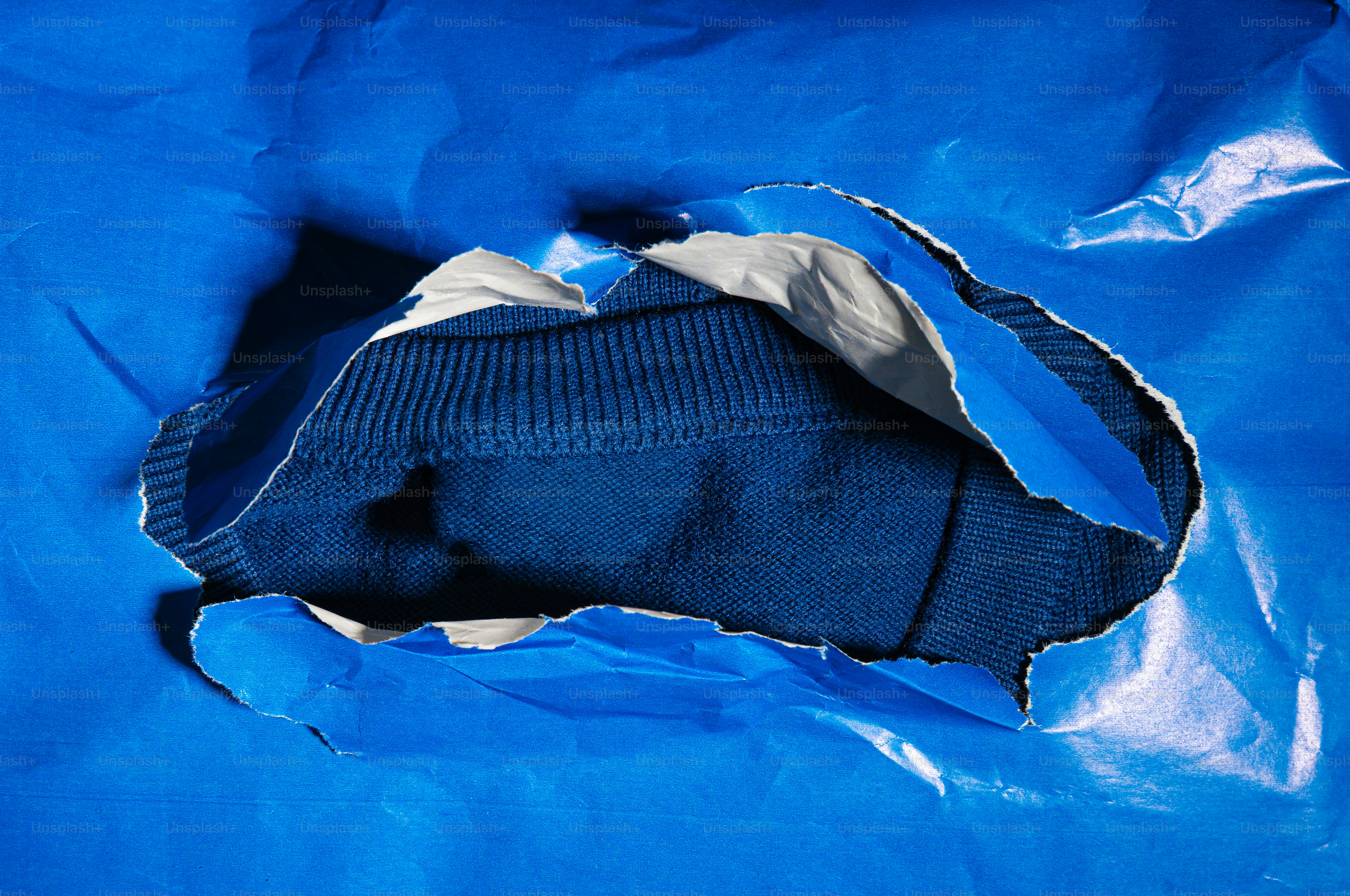 Um suéter azul espiando por entre papel azul rasgado.