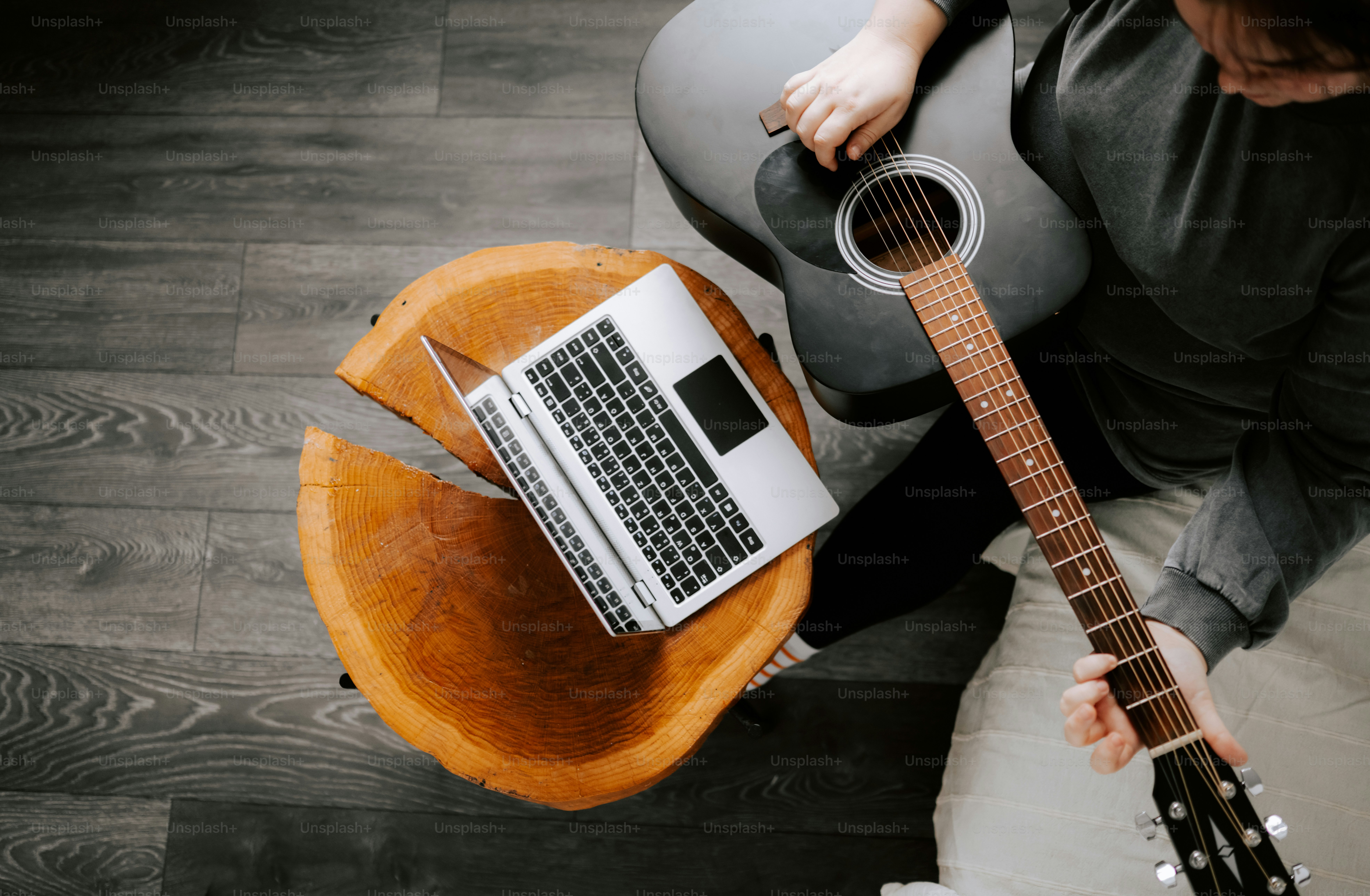Person playing guitar next to laptop on table