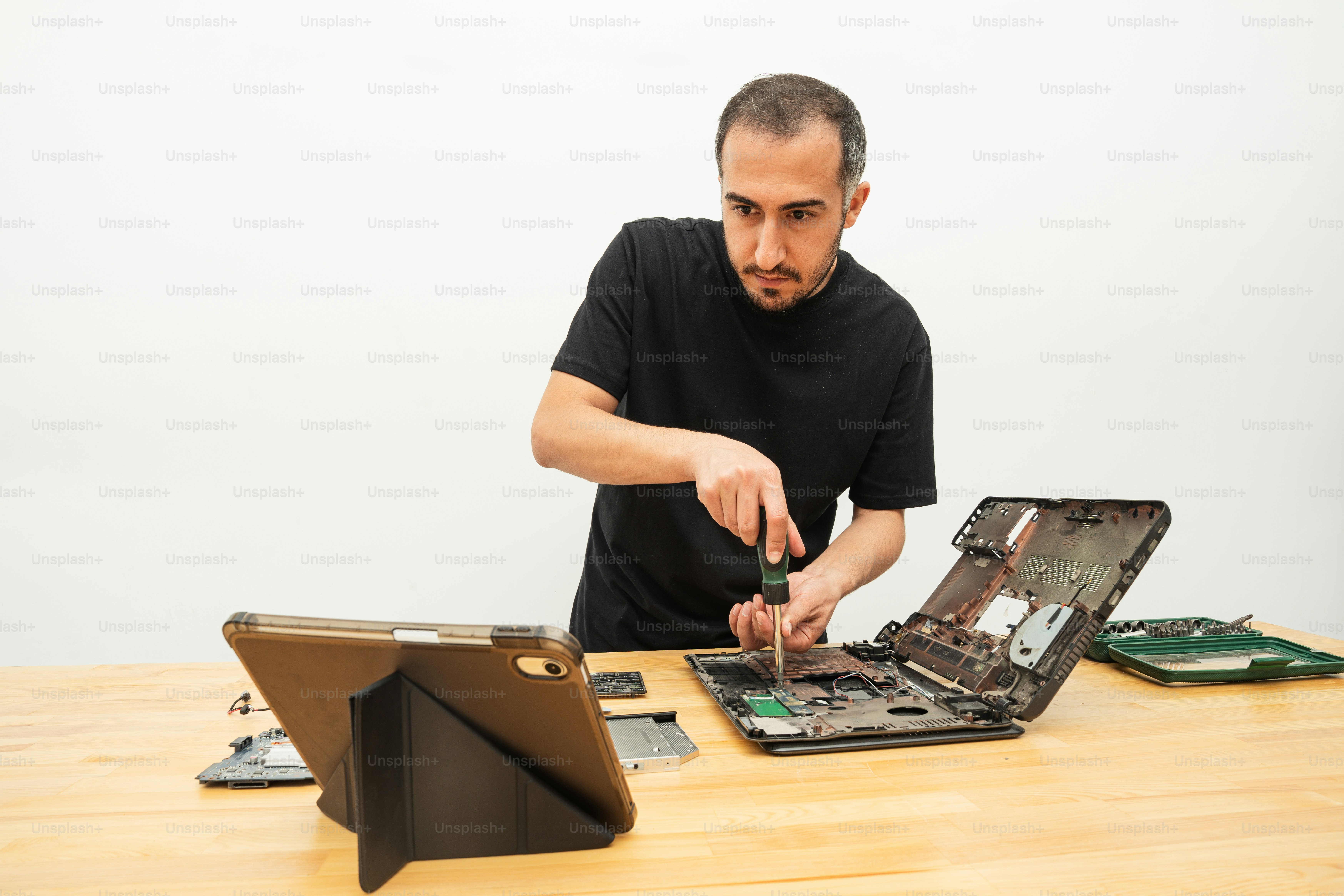 Pria memperbaiki laptop dengan obeng dan tablet