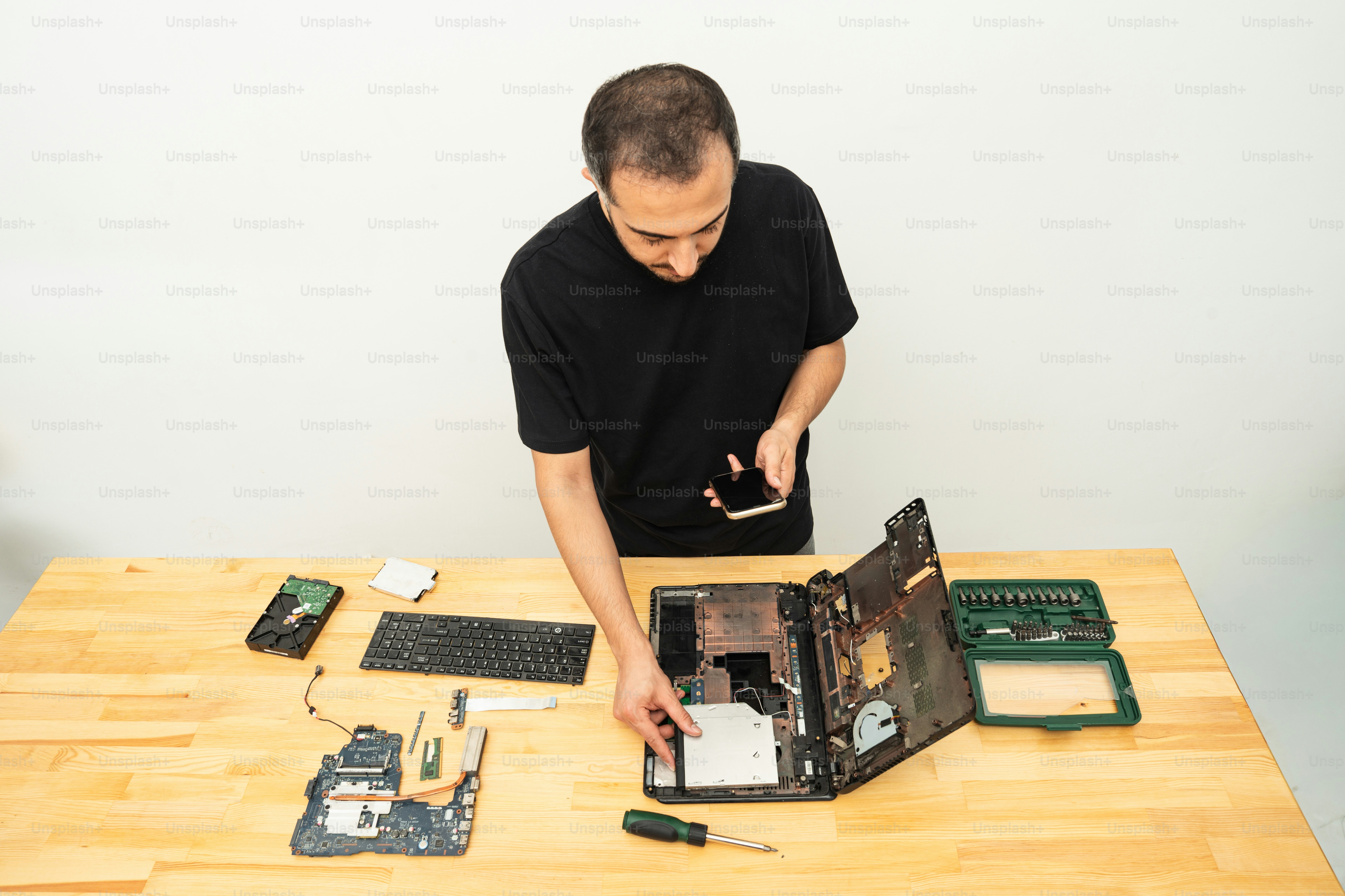 Man repairing a damaged laptop on a wooden table.