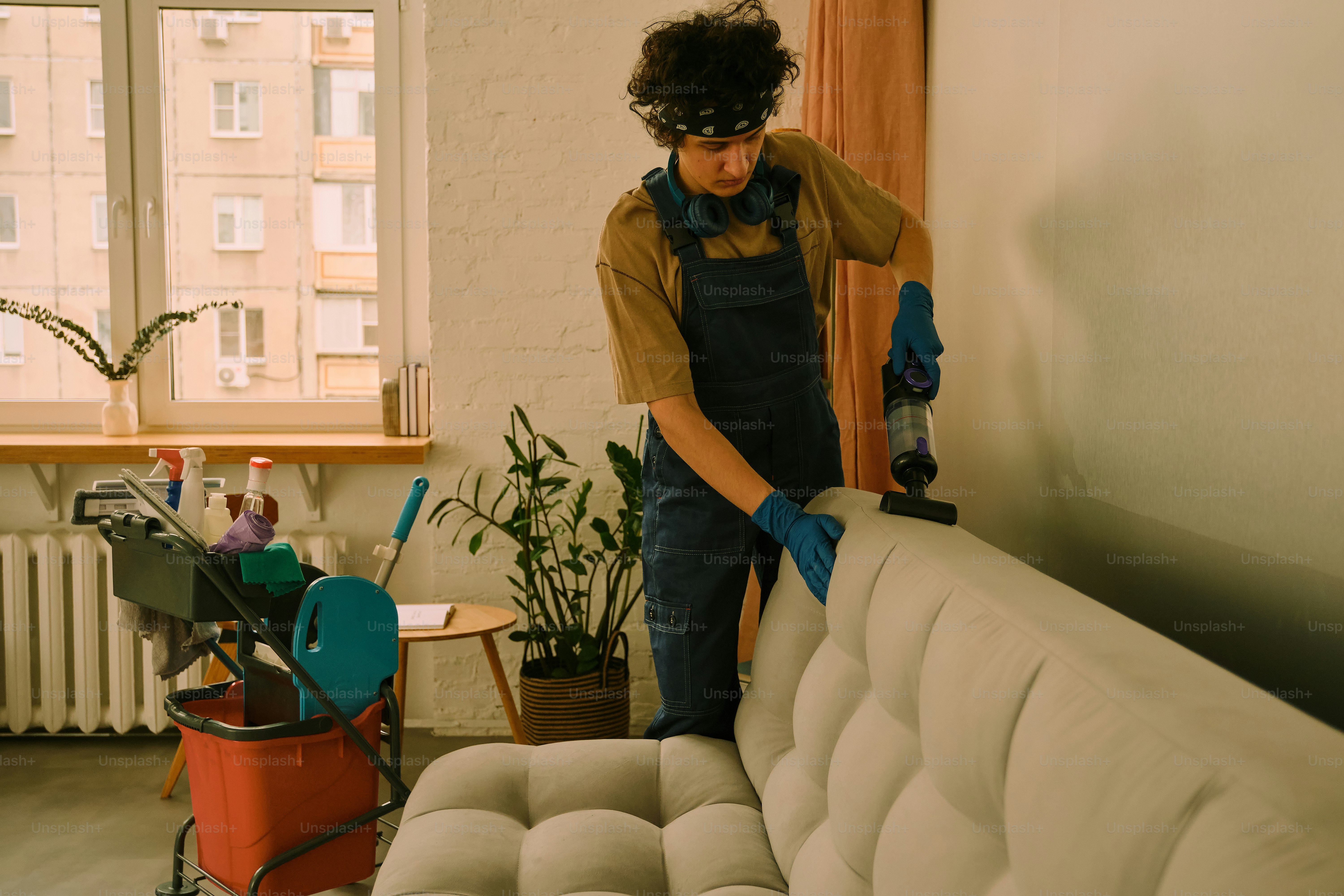 Person vacuuming a tufted sofa in a room.