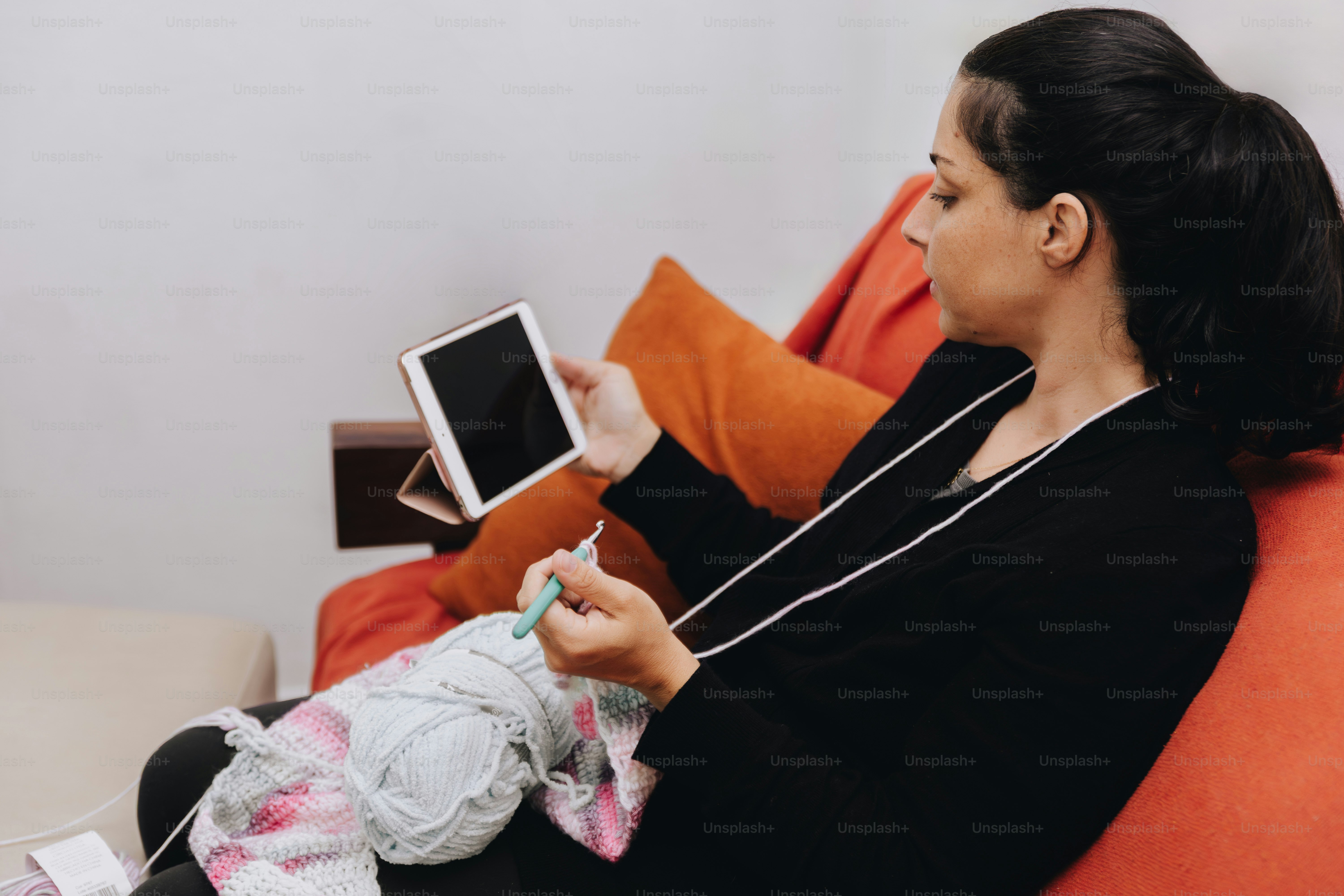 Woman crocheting while watching tablet on tablet