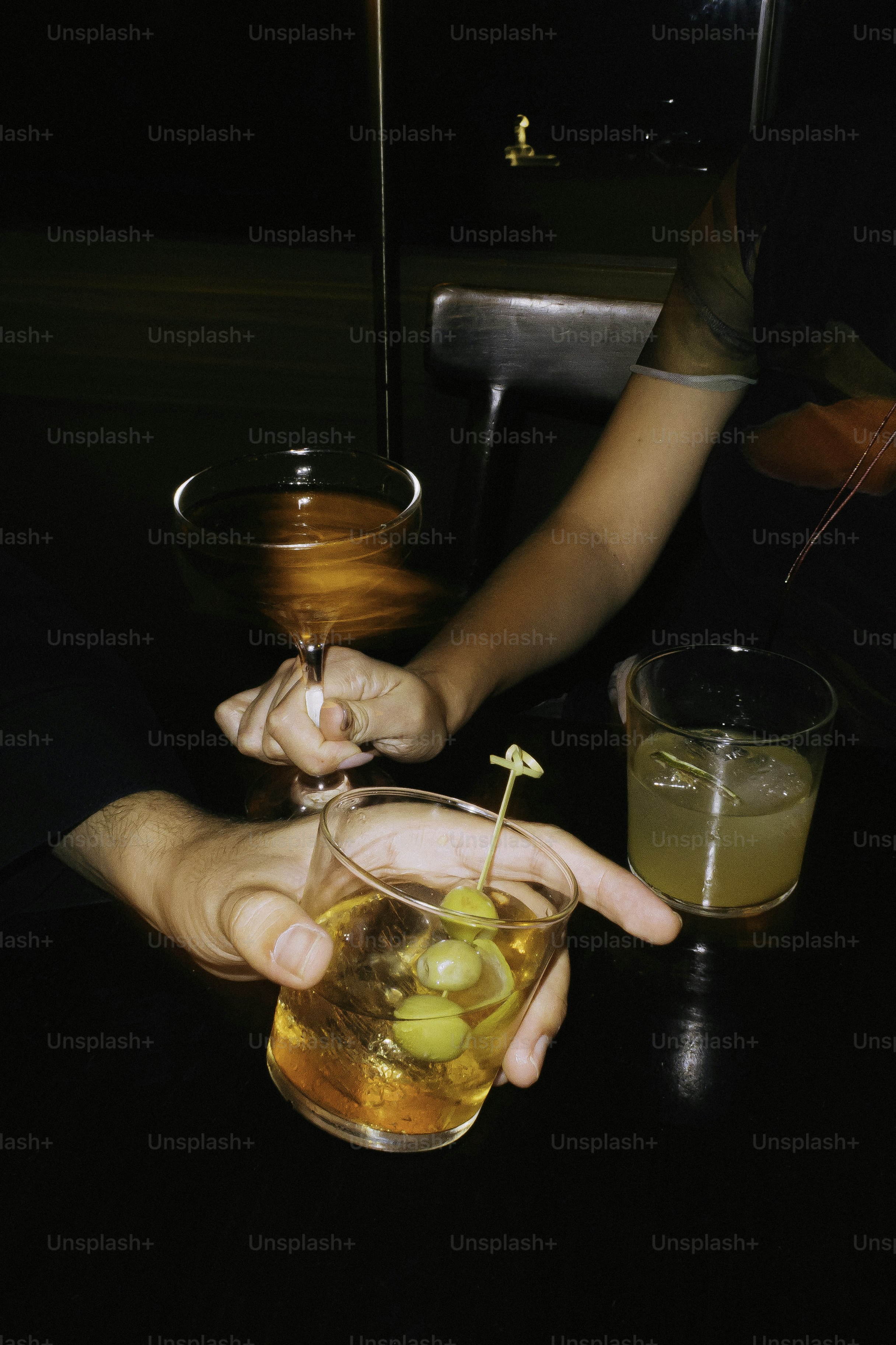 Hands holding cocktails with olives and ice