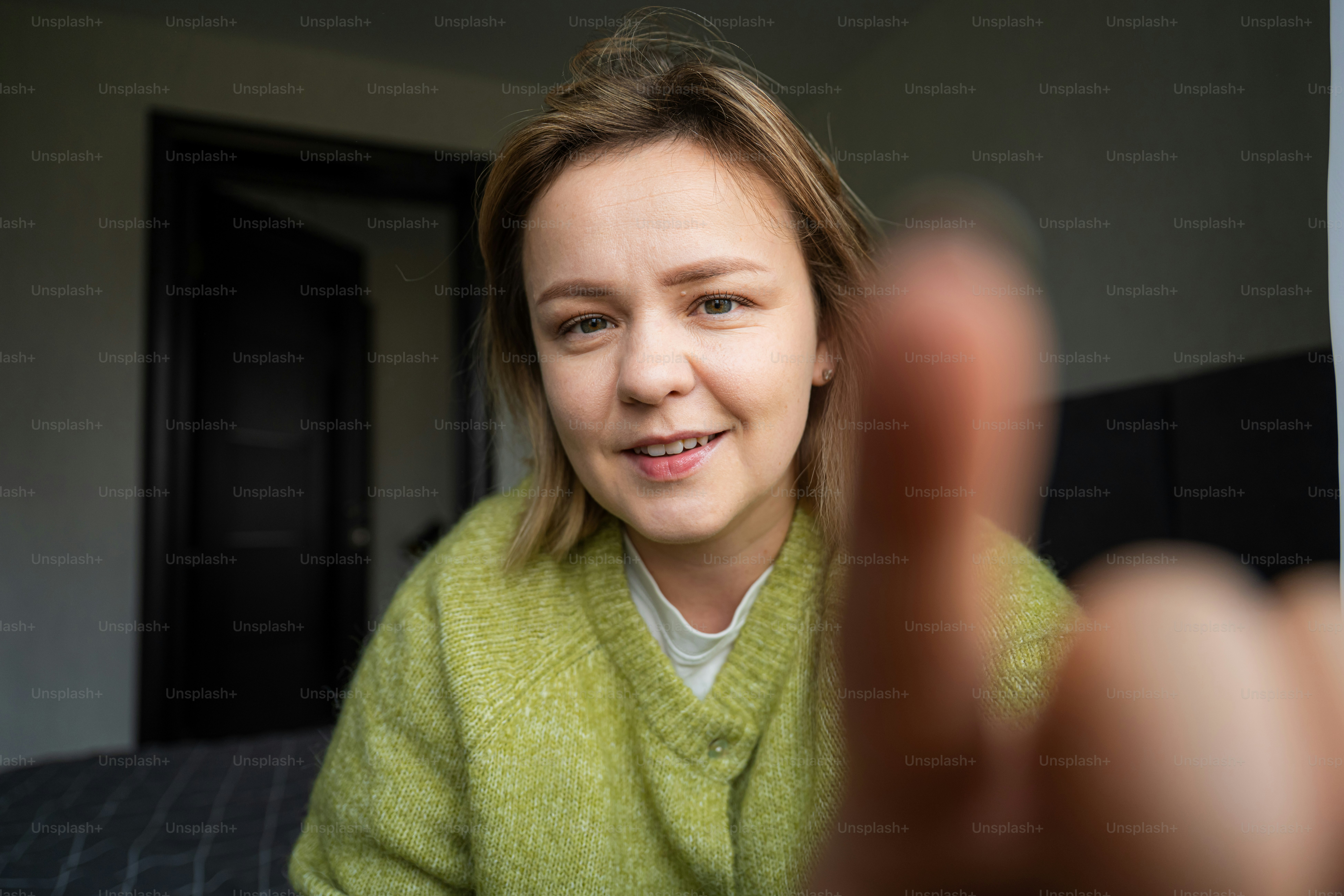 Young woman in green sweater reaching towards camera
