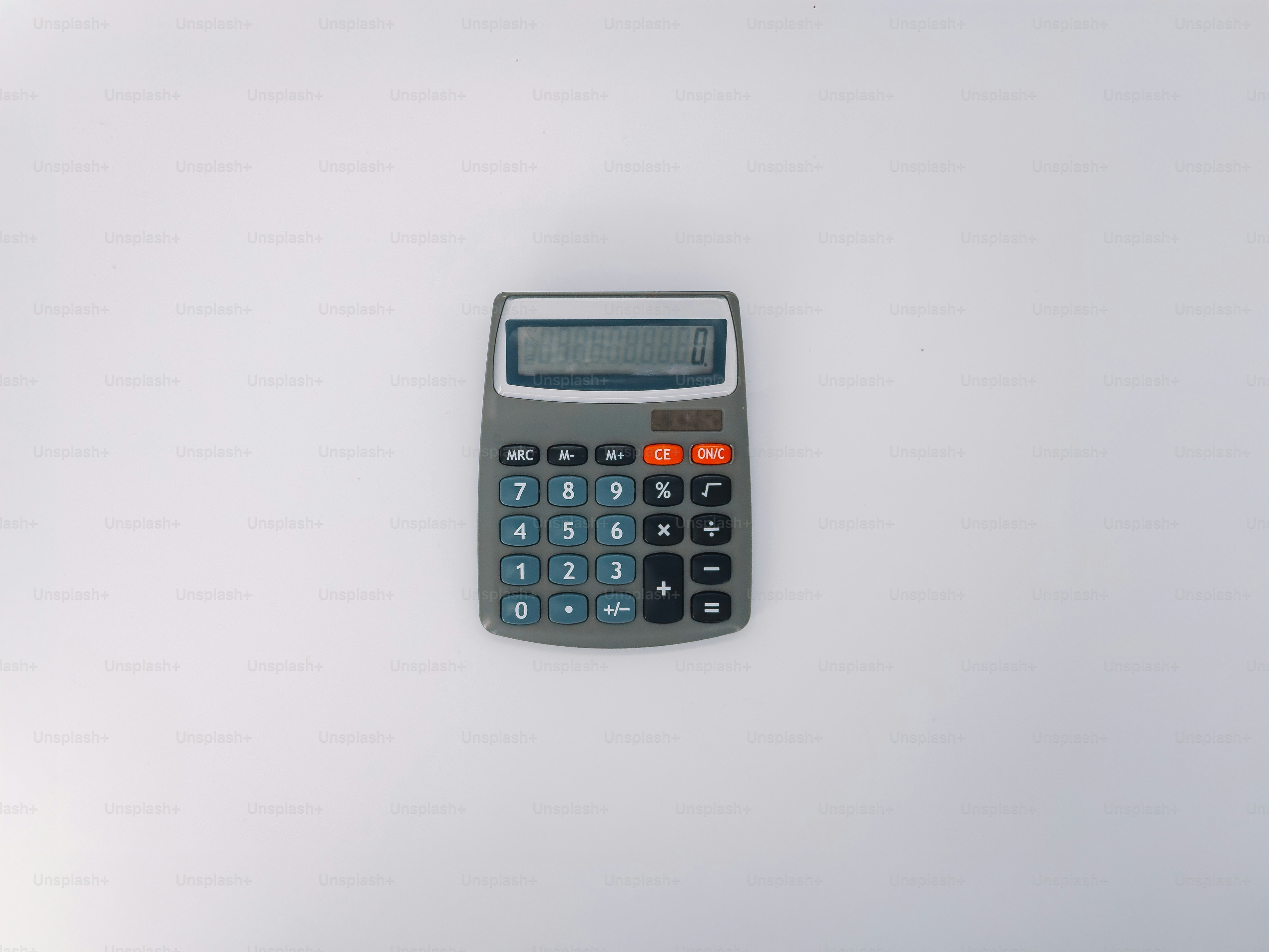 A gray calculator sits on a white surface.