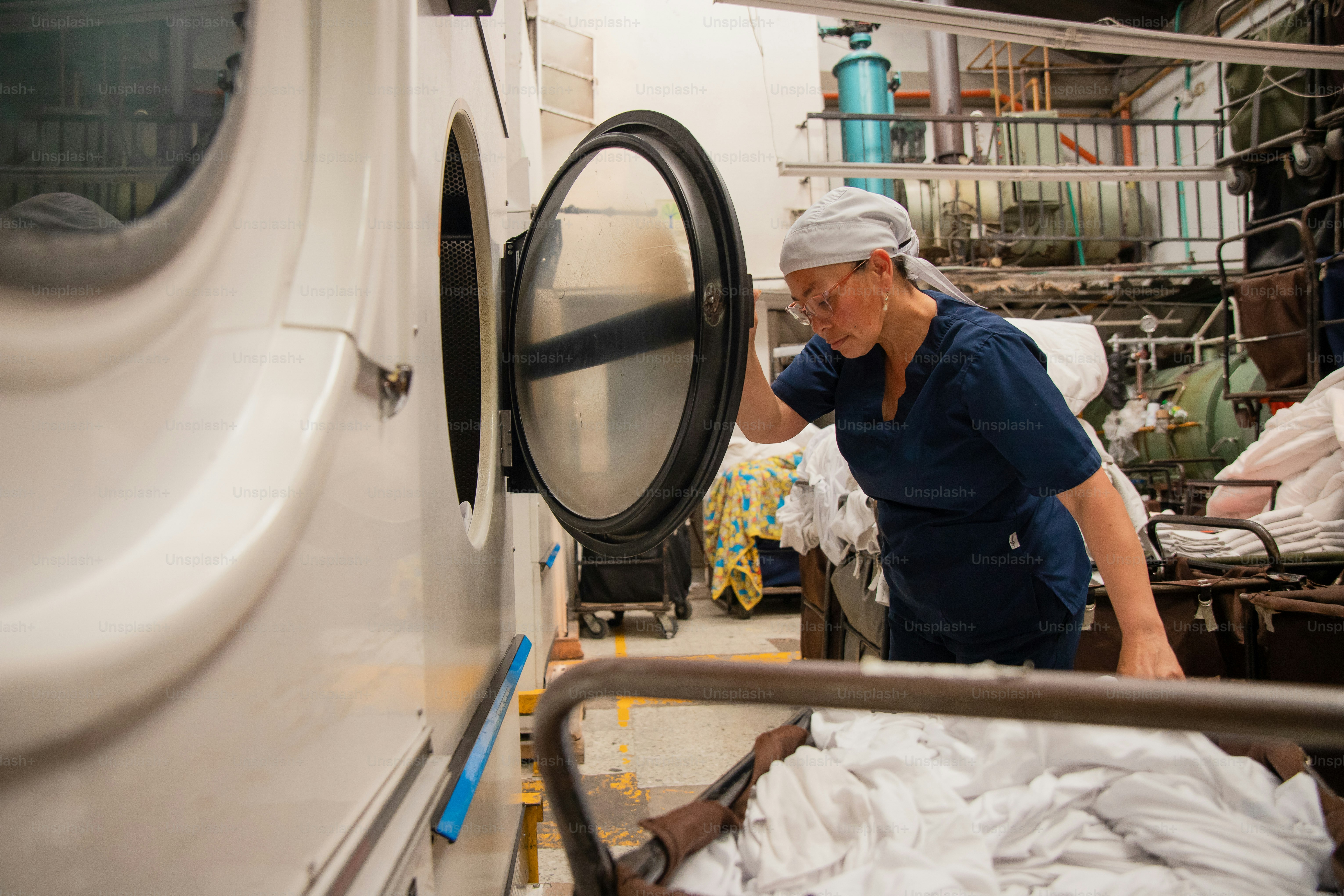 Woman operating industrial laundry machine with white sheets photo ...