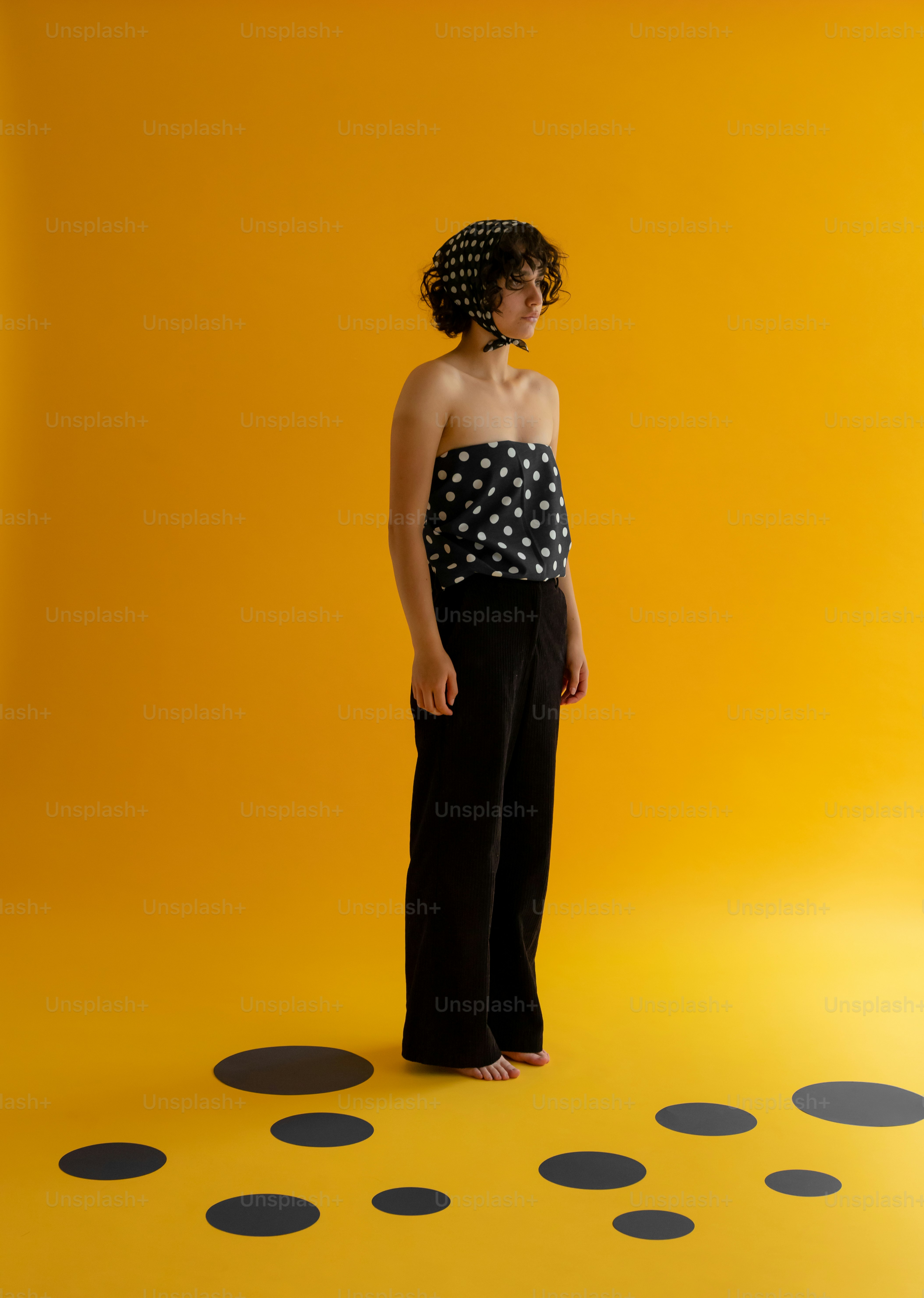 Frau mit gepunktetem Oberteil und schwarzer Hose auf gelber Bühne