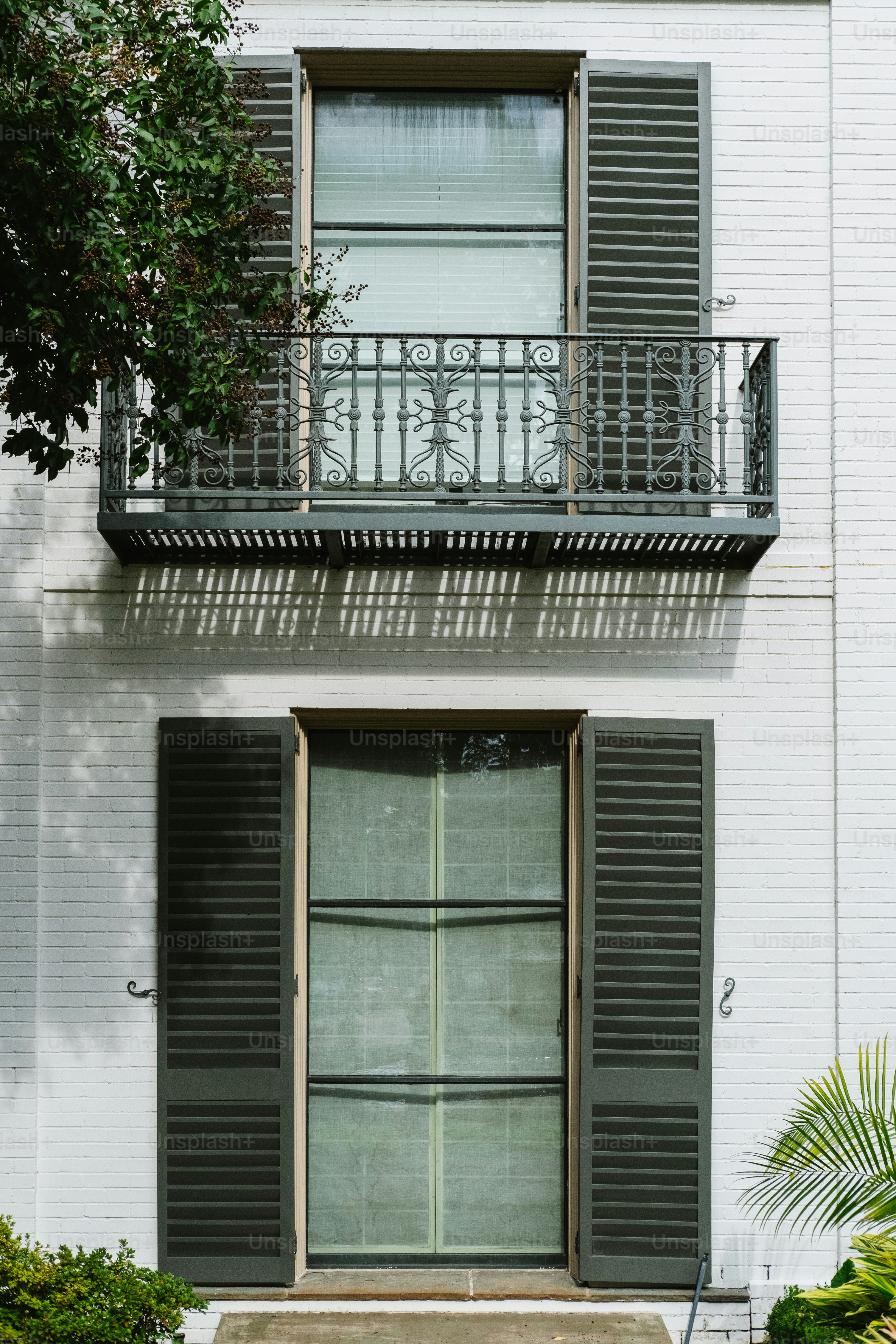 Weißes Backsteingebäude mit dunklen Fensterläden und Balkon.
