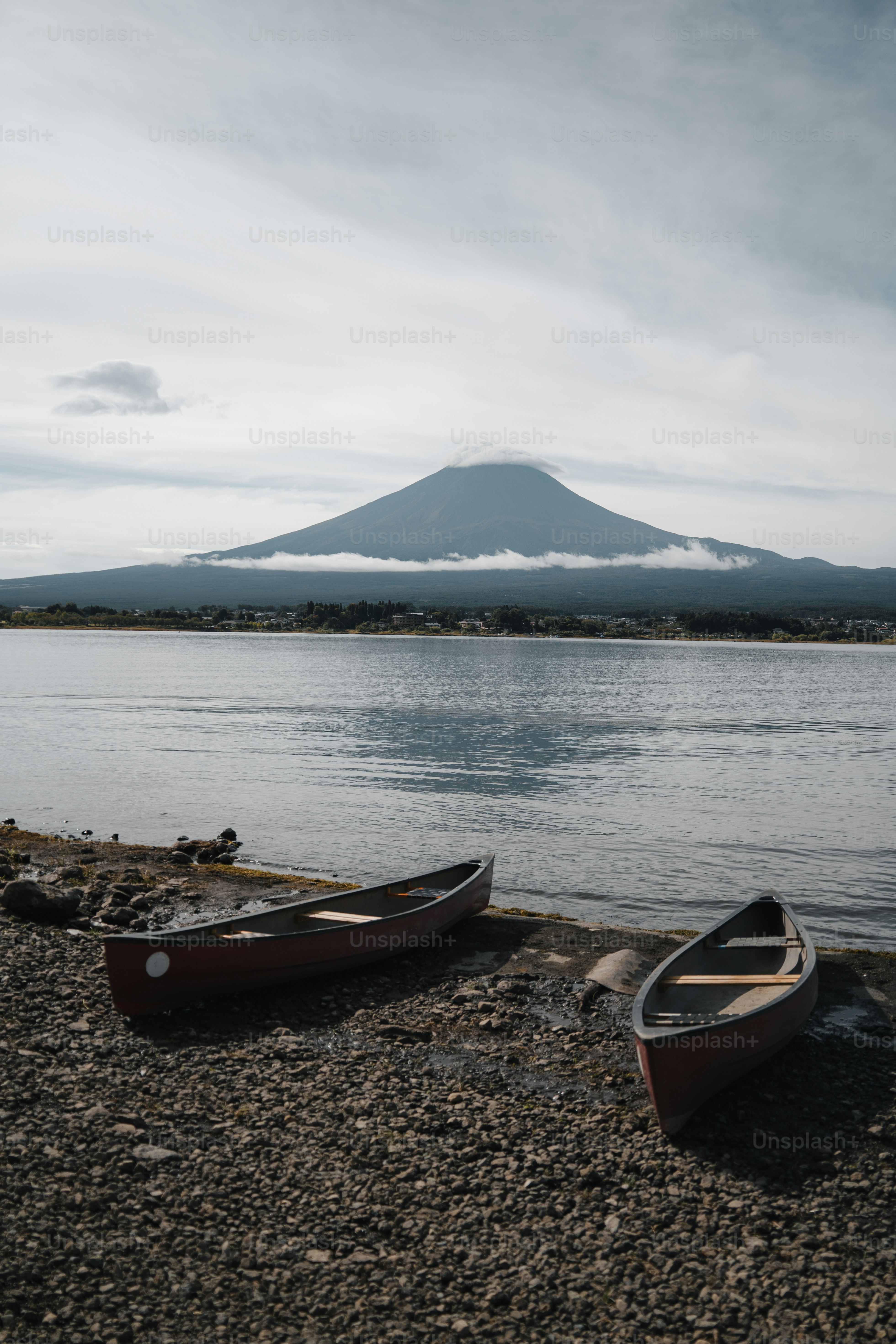 Two canoes rest on a rocky shore with mount fuji.