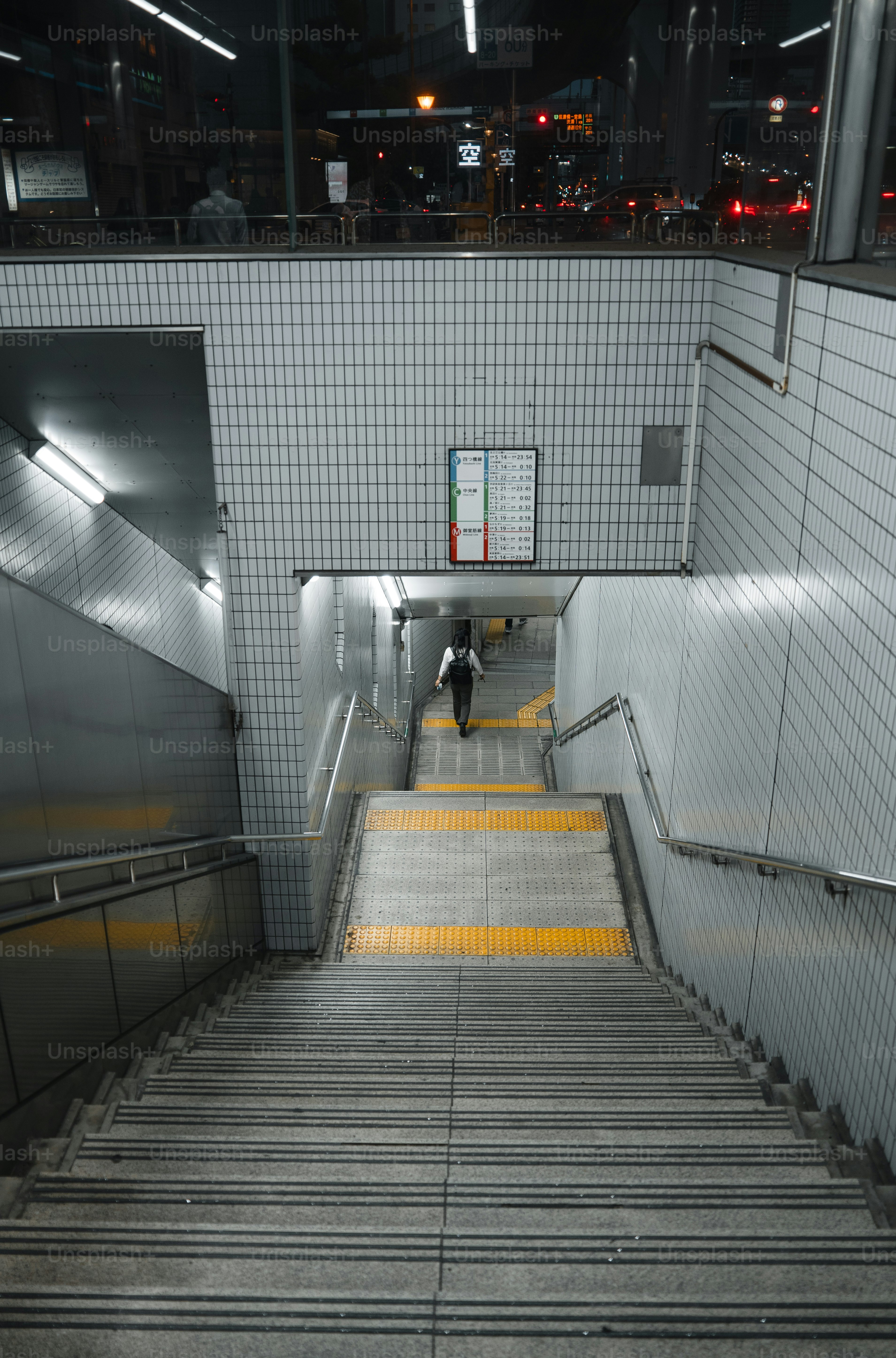 A person walks down a subway station staircase at night.