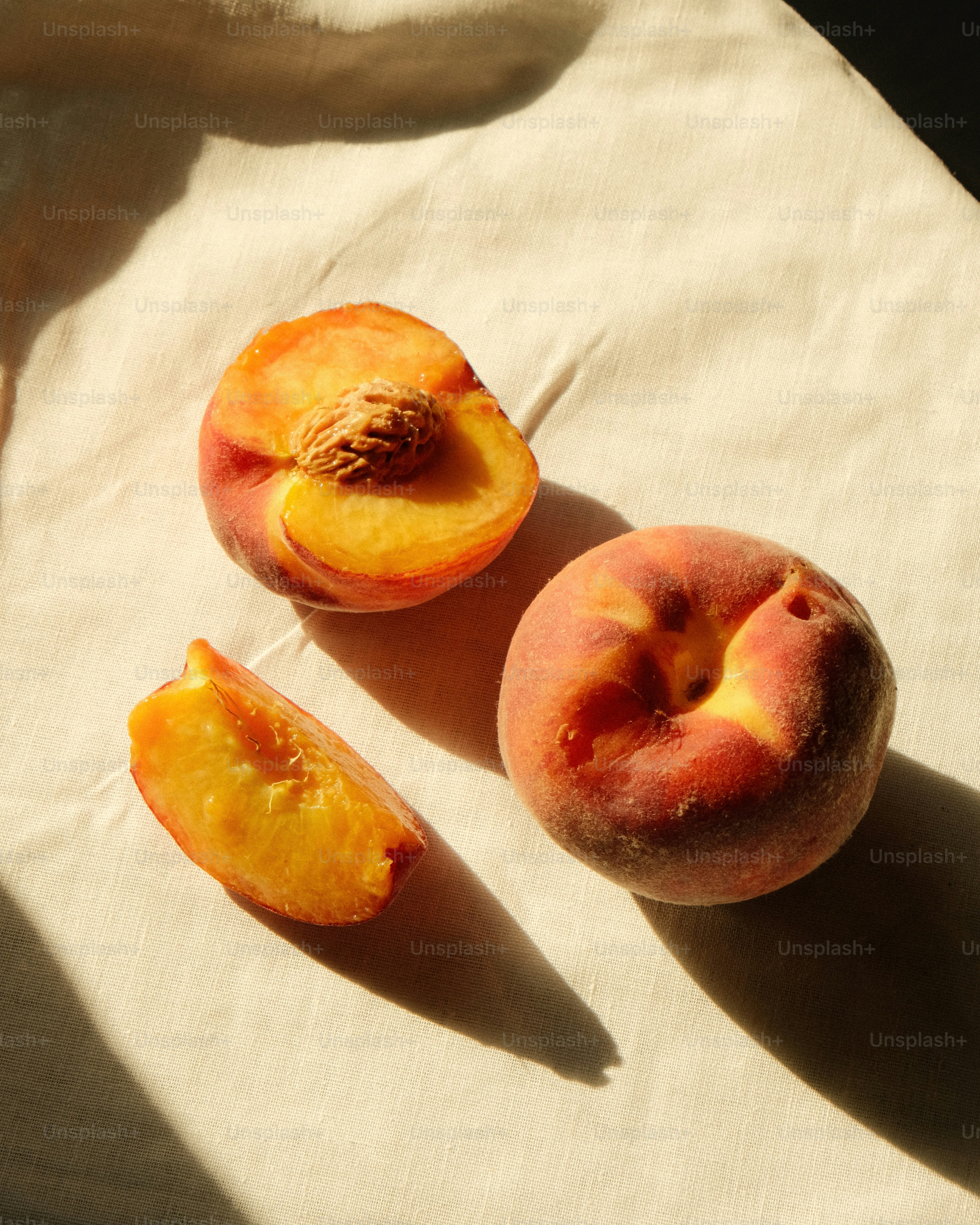 Whole and sliced peaches on a white cloth.