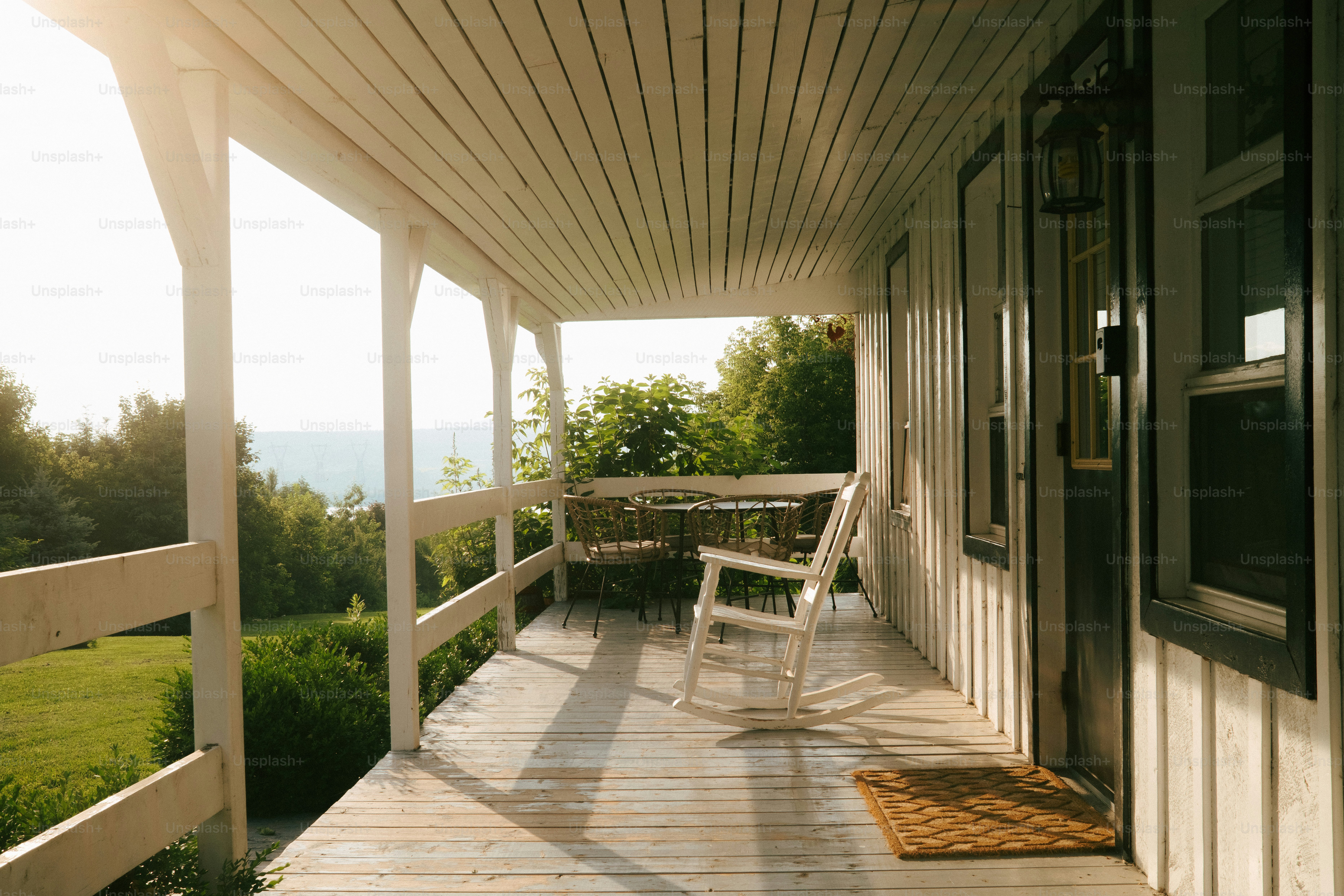 White rocking chair on a sunlit porch overlooking greenery