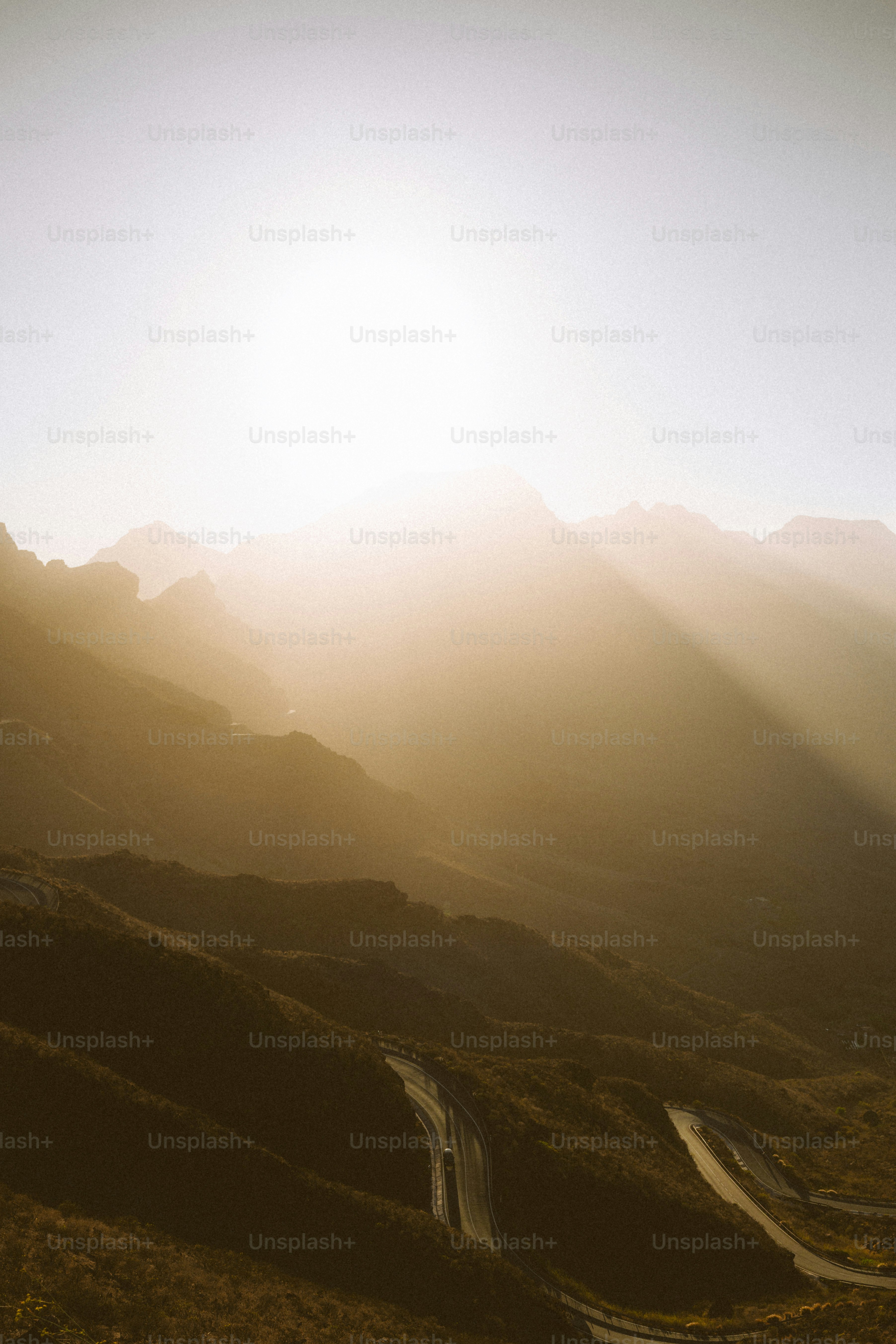 Sunbeams illuminate winding road through mountainous terrain.