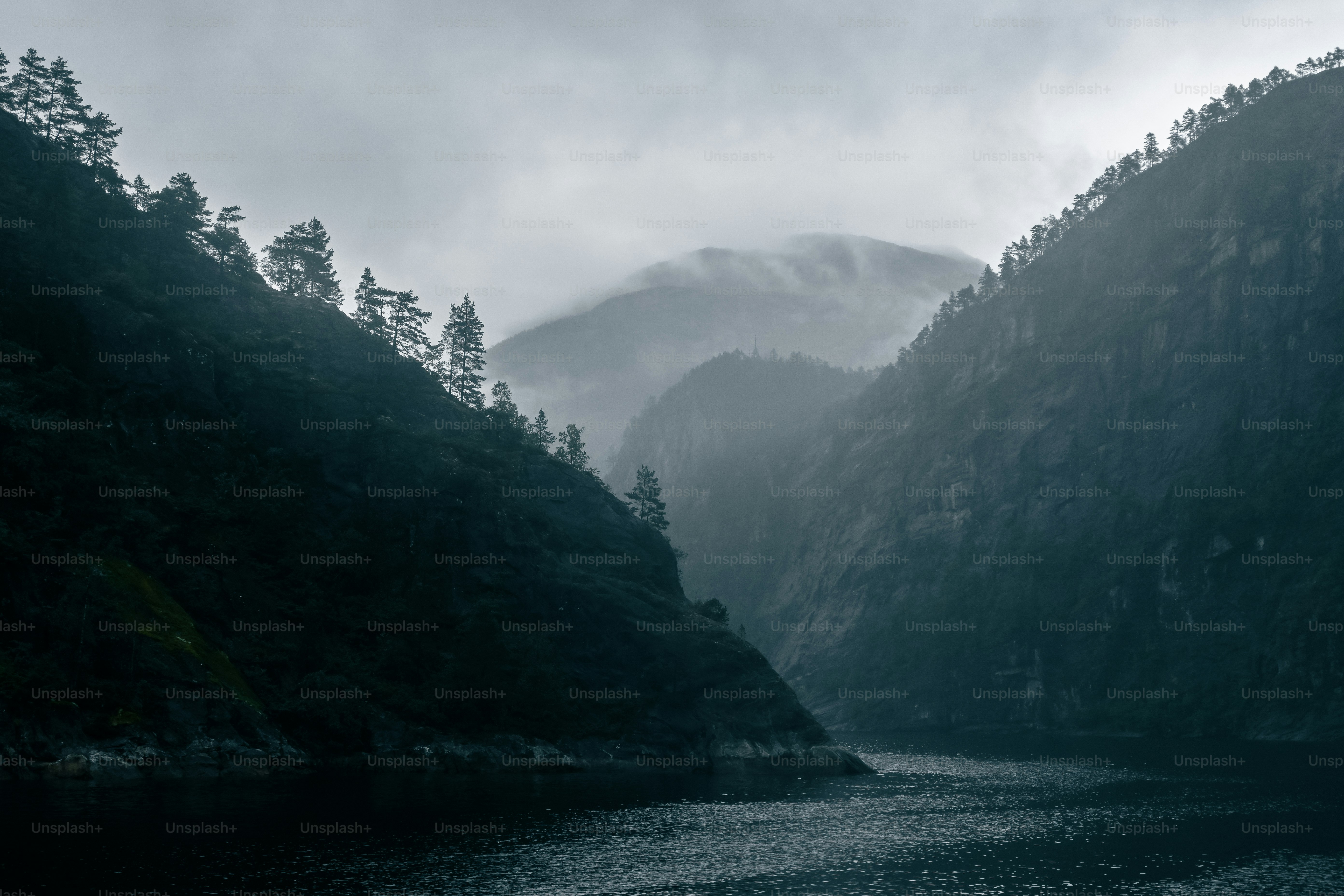 Montagne nebbiose si innalzano sopra un specchio d'acqua scuro e calmo.