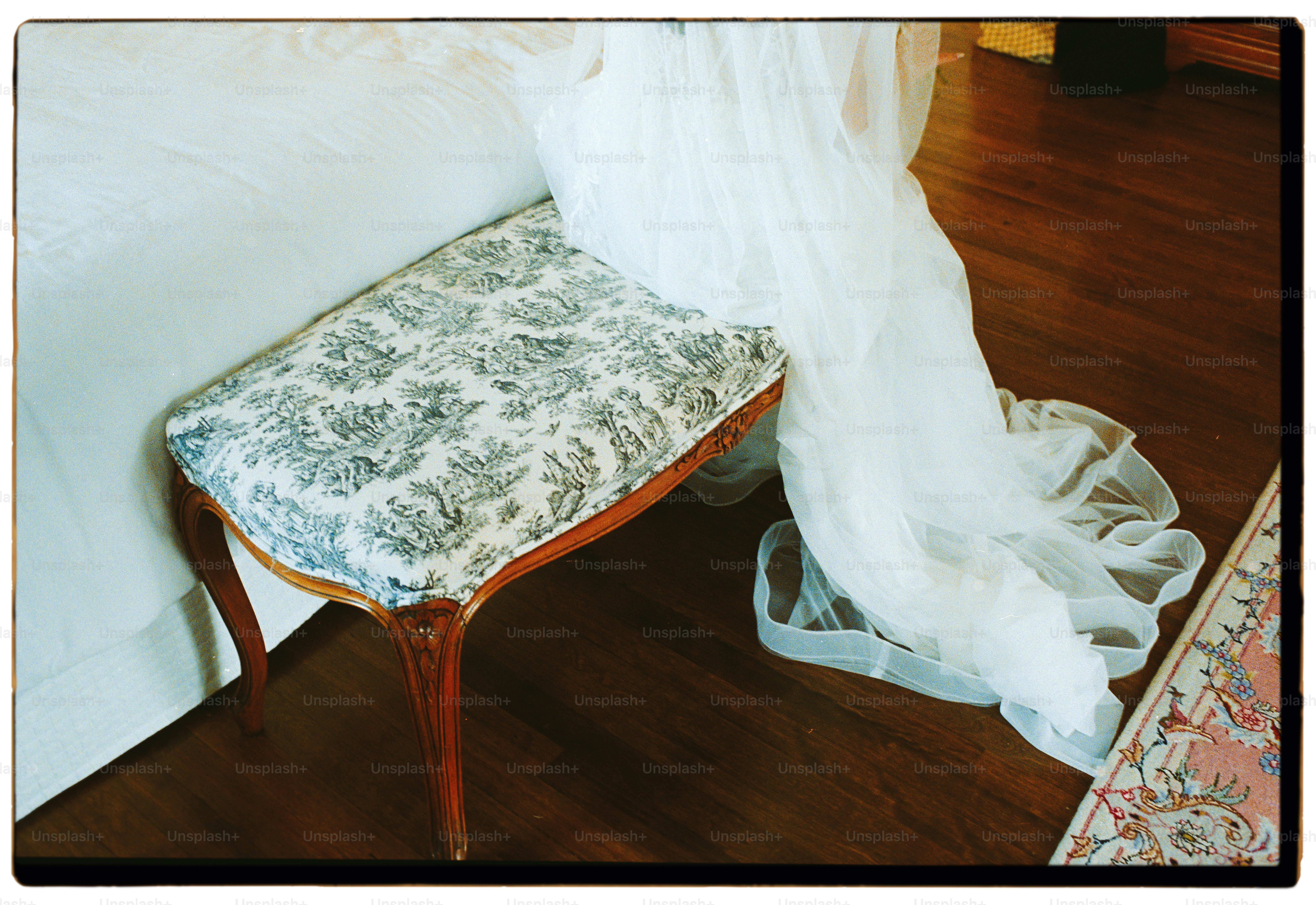 Upholstered bench with floral pattern next to sheer fabric.