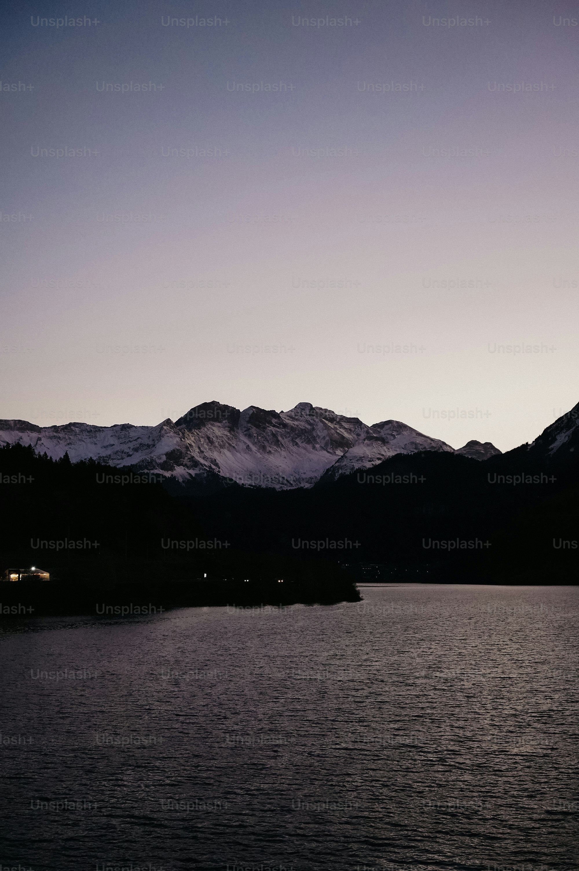 Des montagnes enneigées au crépuscule au-dessus d’un lac calme.