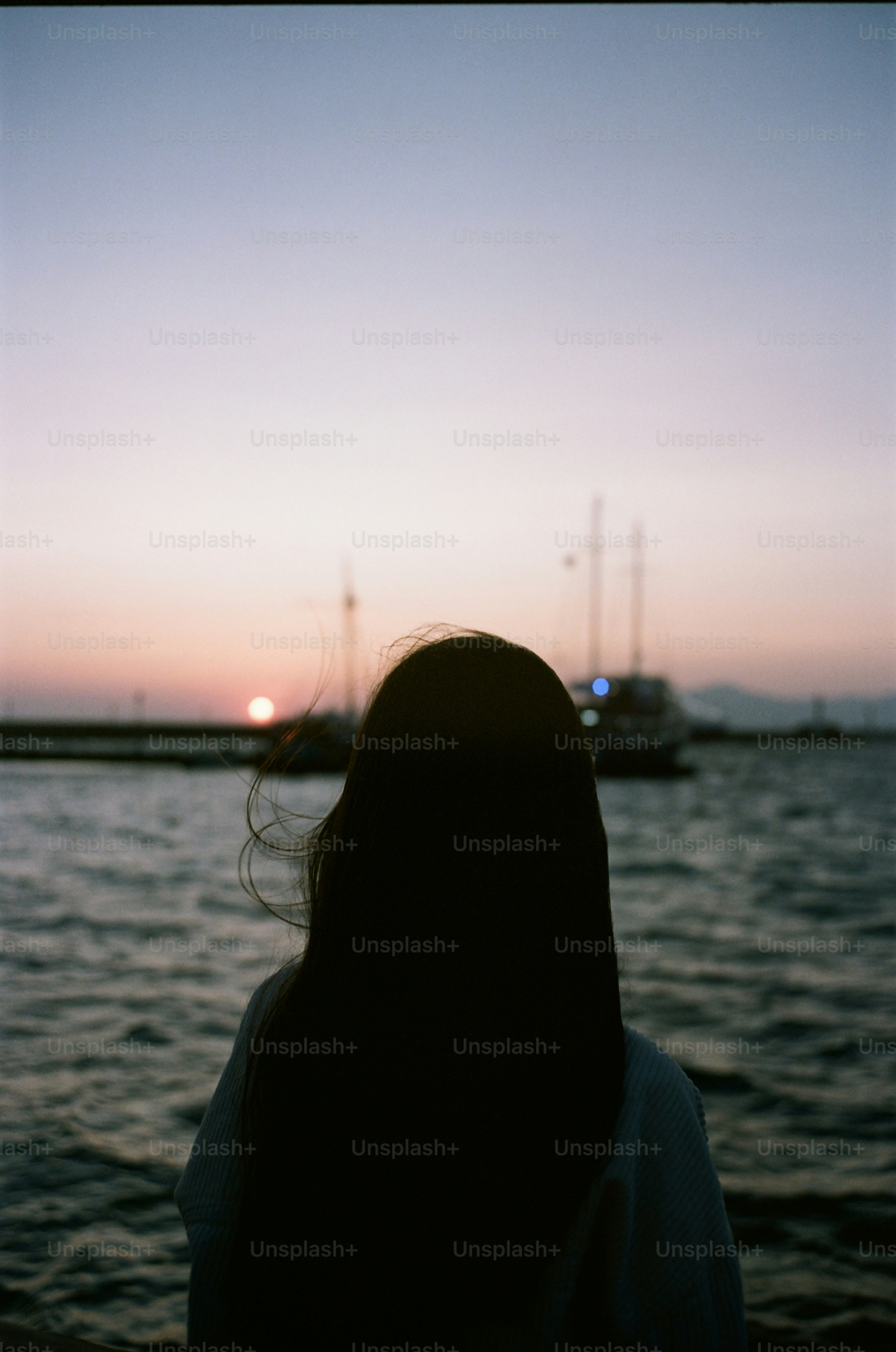 Une femme regarde le coucher du soleil sur l’océan avec des bateaux.