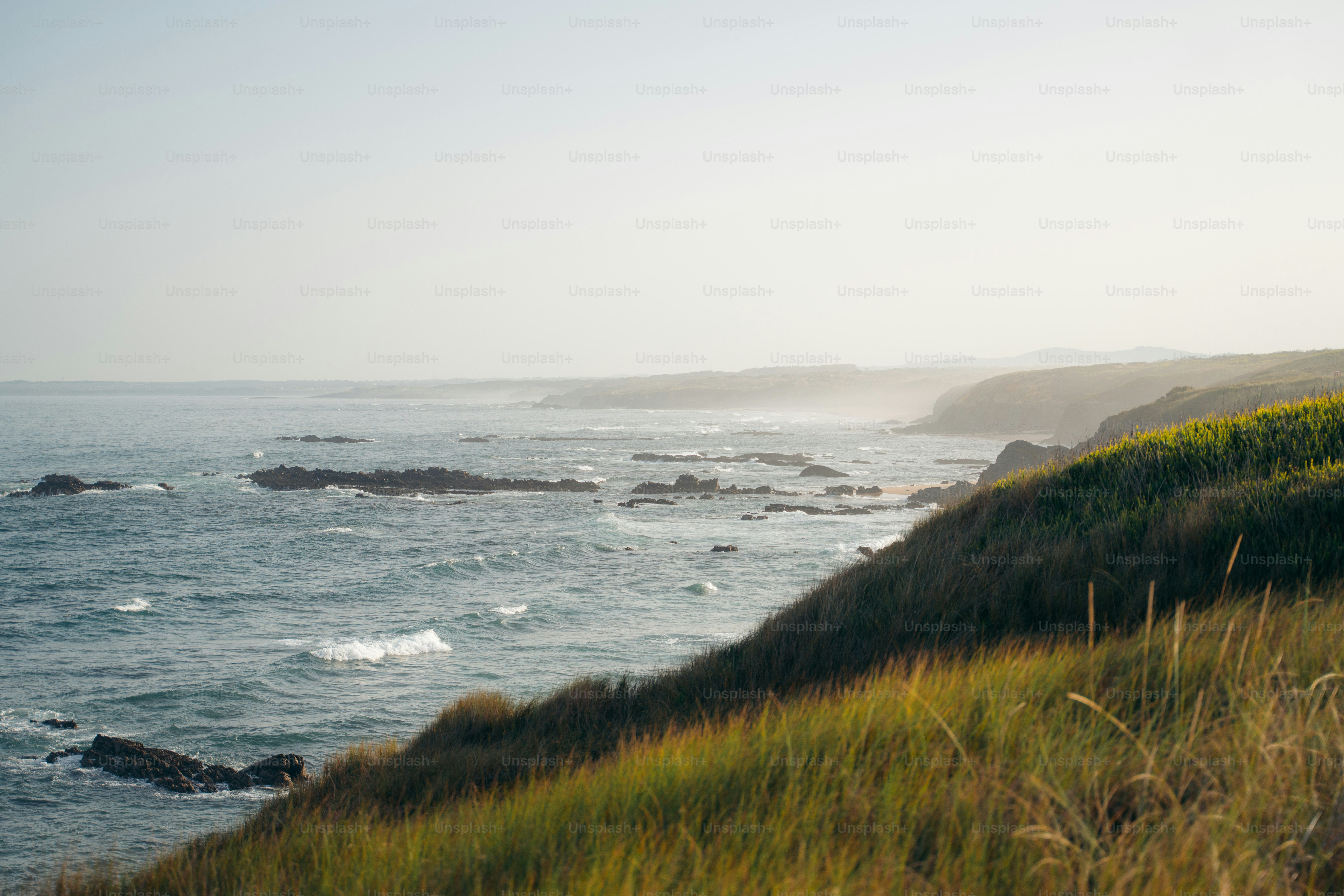 Les vagues de l’océan s’écrasent sur le rivage rocheux avec une colline herbeuse.