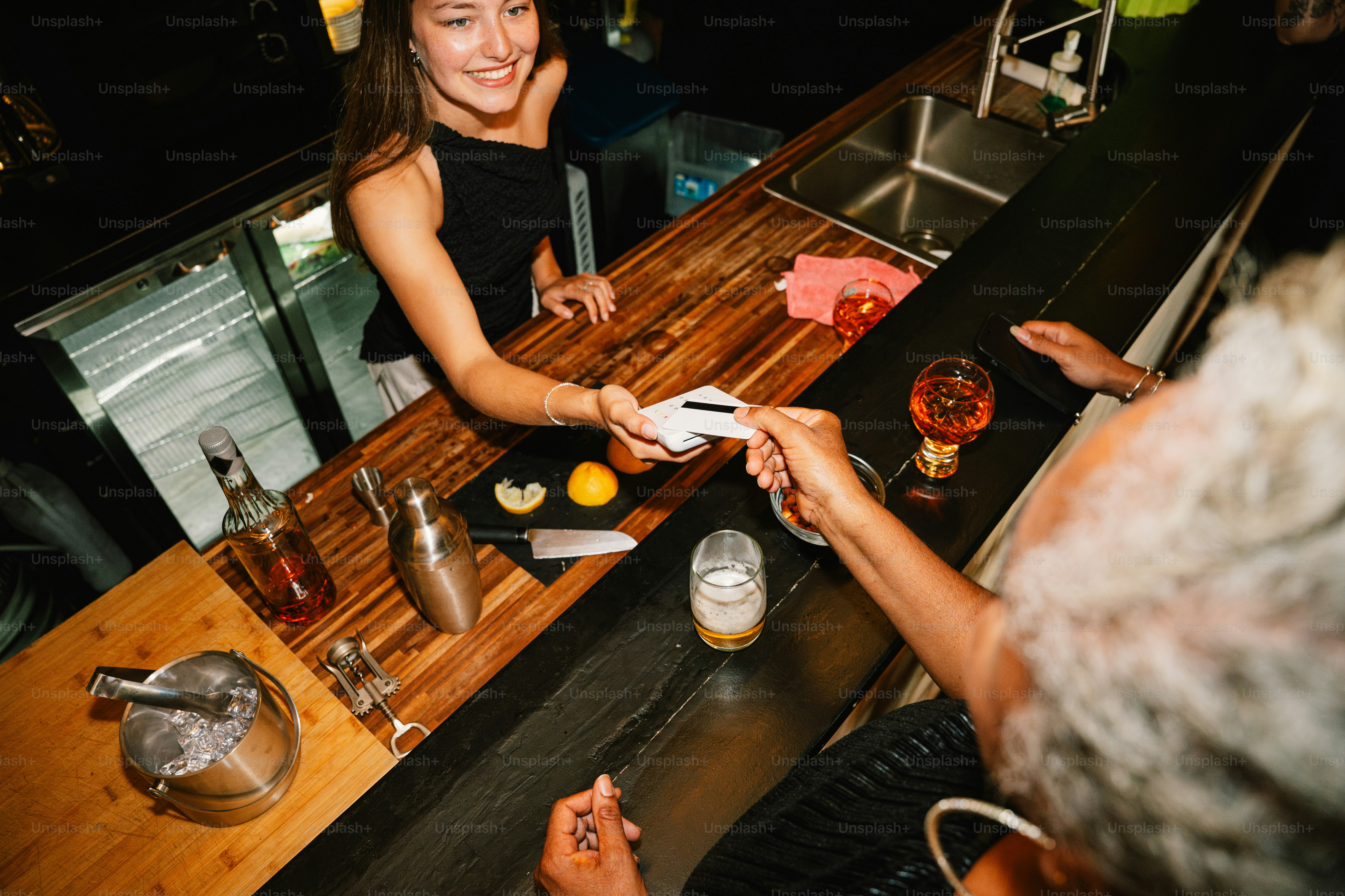 A smiling bartender prepares a drink behind a bar. photo – Drinks Image ...