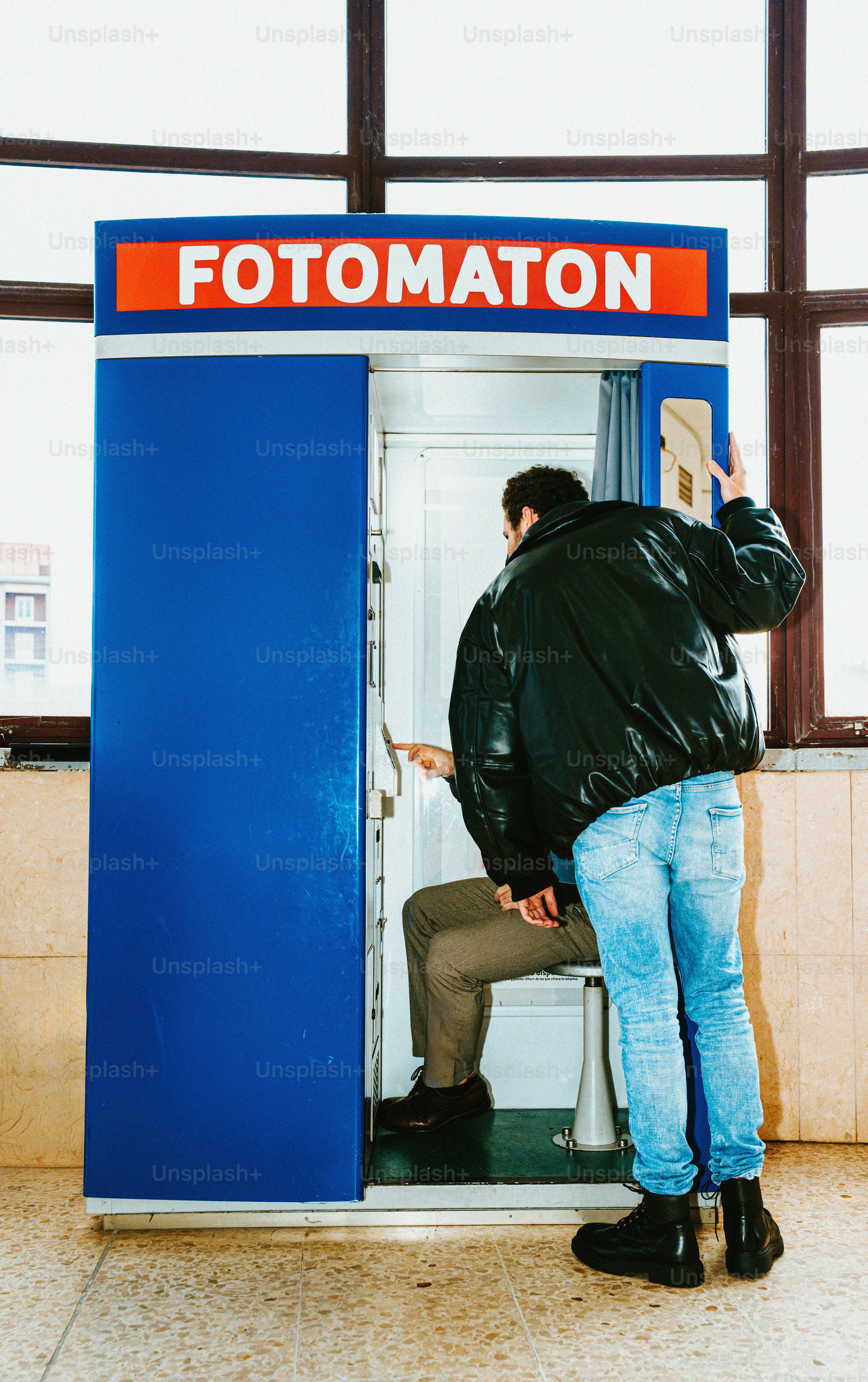 Two men using a photo booth with "fotomaton" sign.