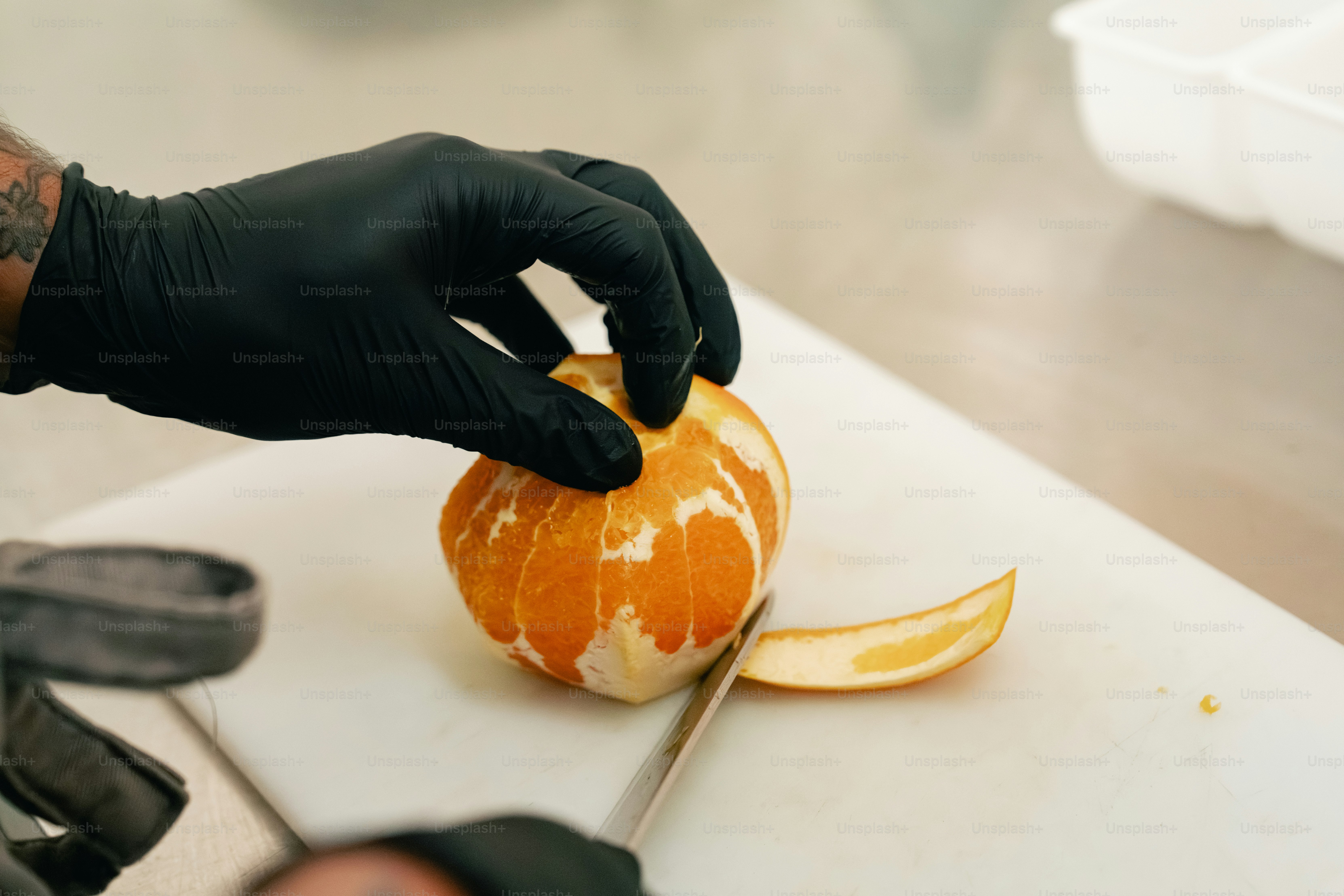 Hands in black gloves peeling an orange on cutting board
