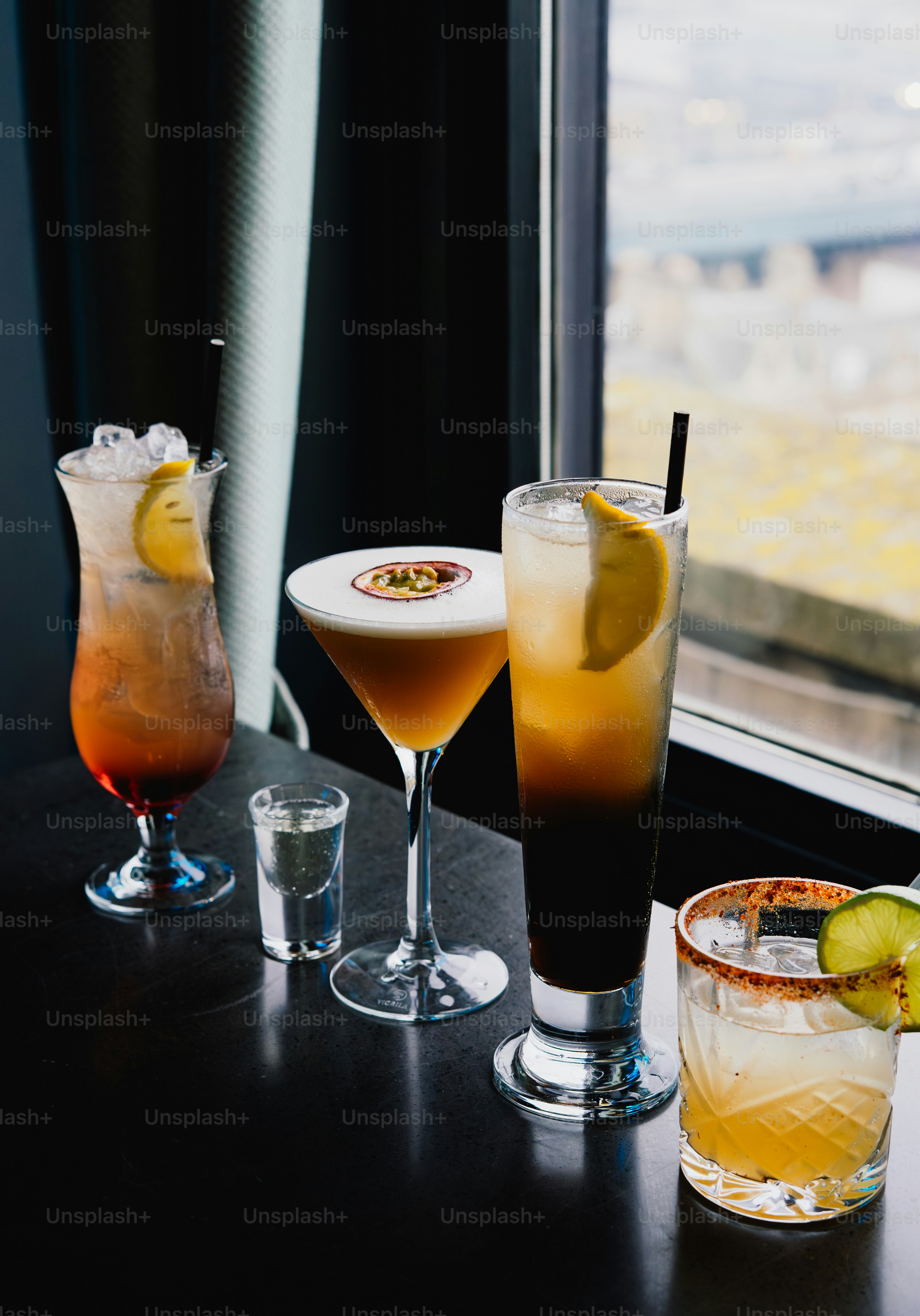 Four colorful cocktails and a shot glass on a table.