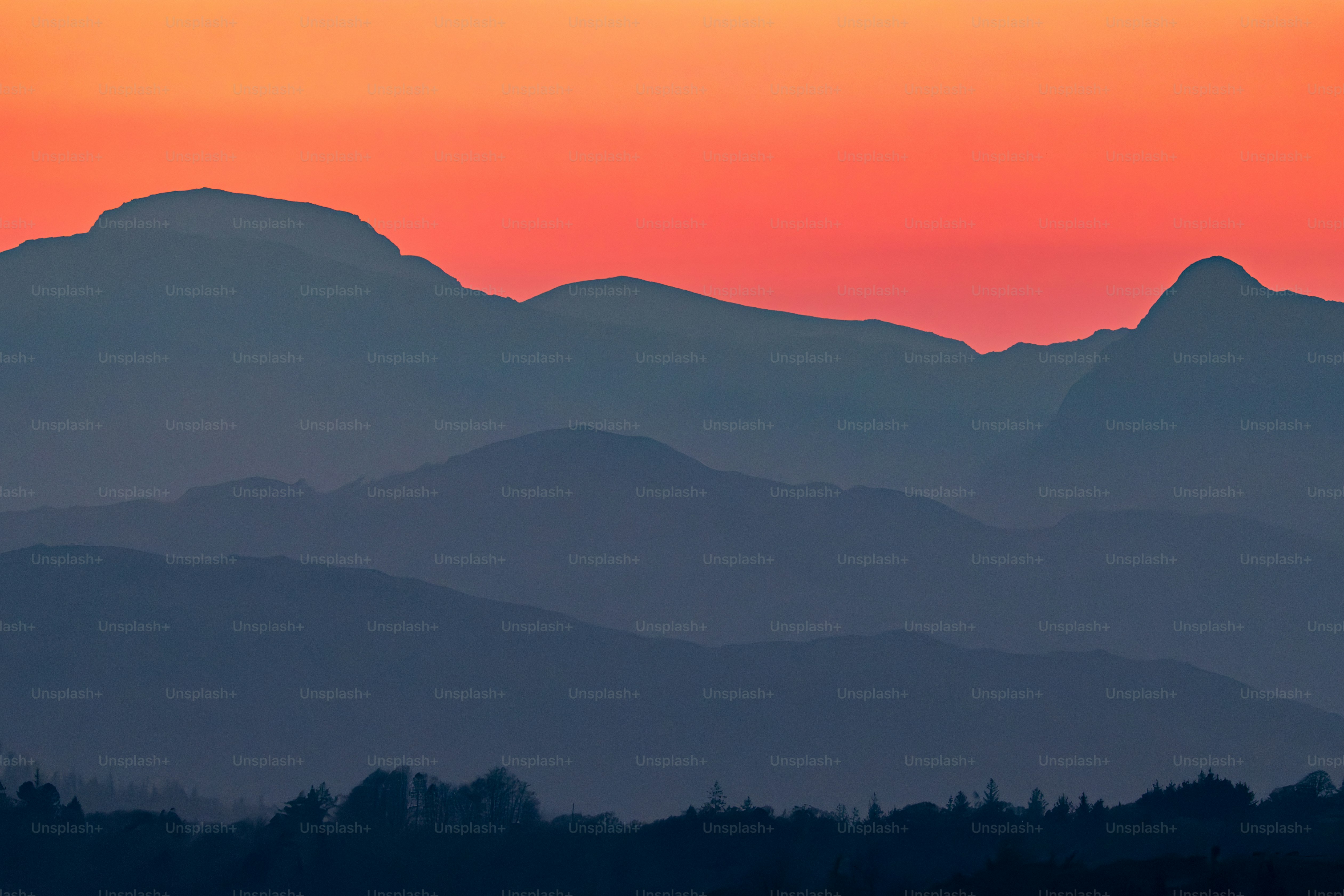 Silhouettenhafte Gebirgszüge vor einem orangefarbenen Sonnenuntergangshimmel