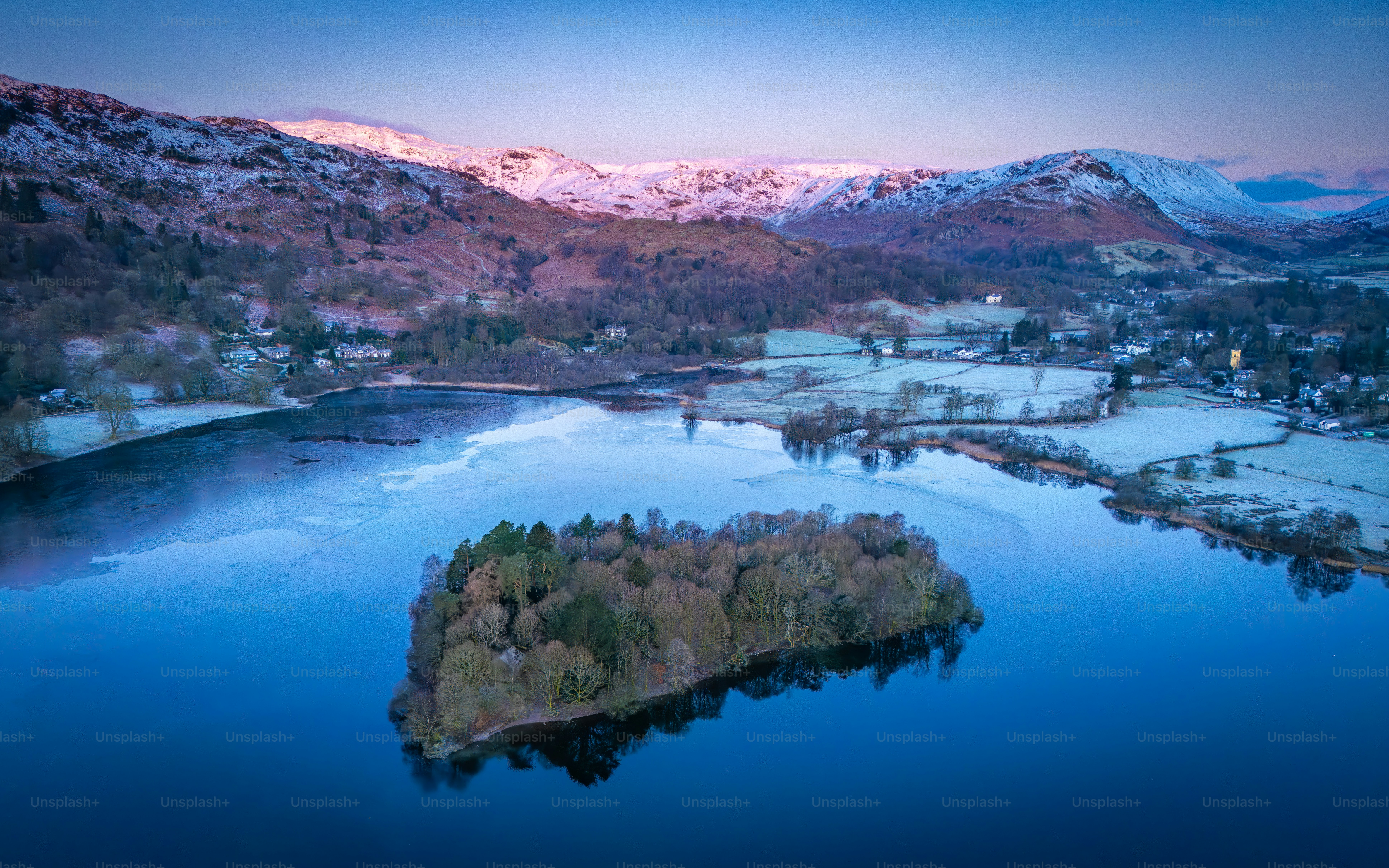 Schneebedeckte Berge blicken bei Tagesanbruch auf einen zugefrorenen Inselsee.