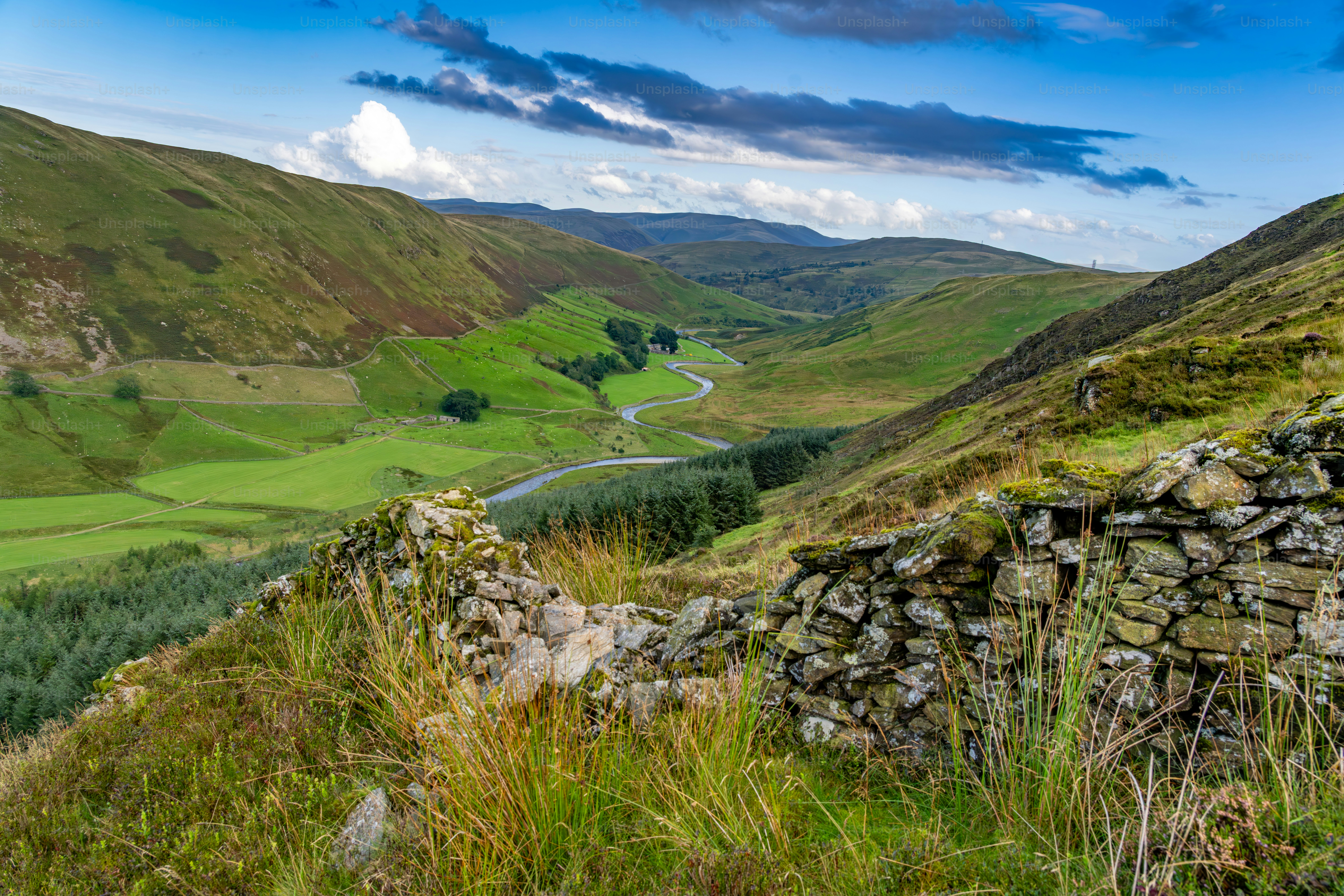 Rolling green hills with a winding river and stone ruins