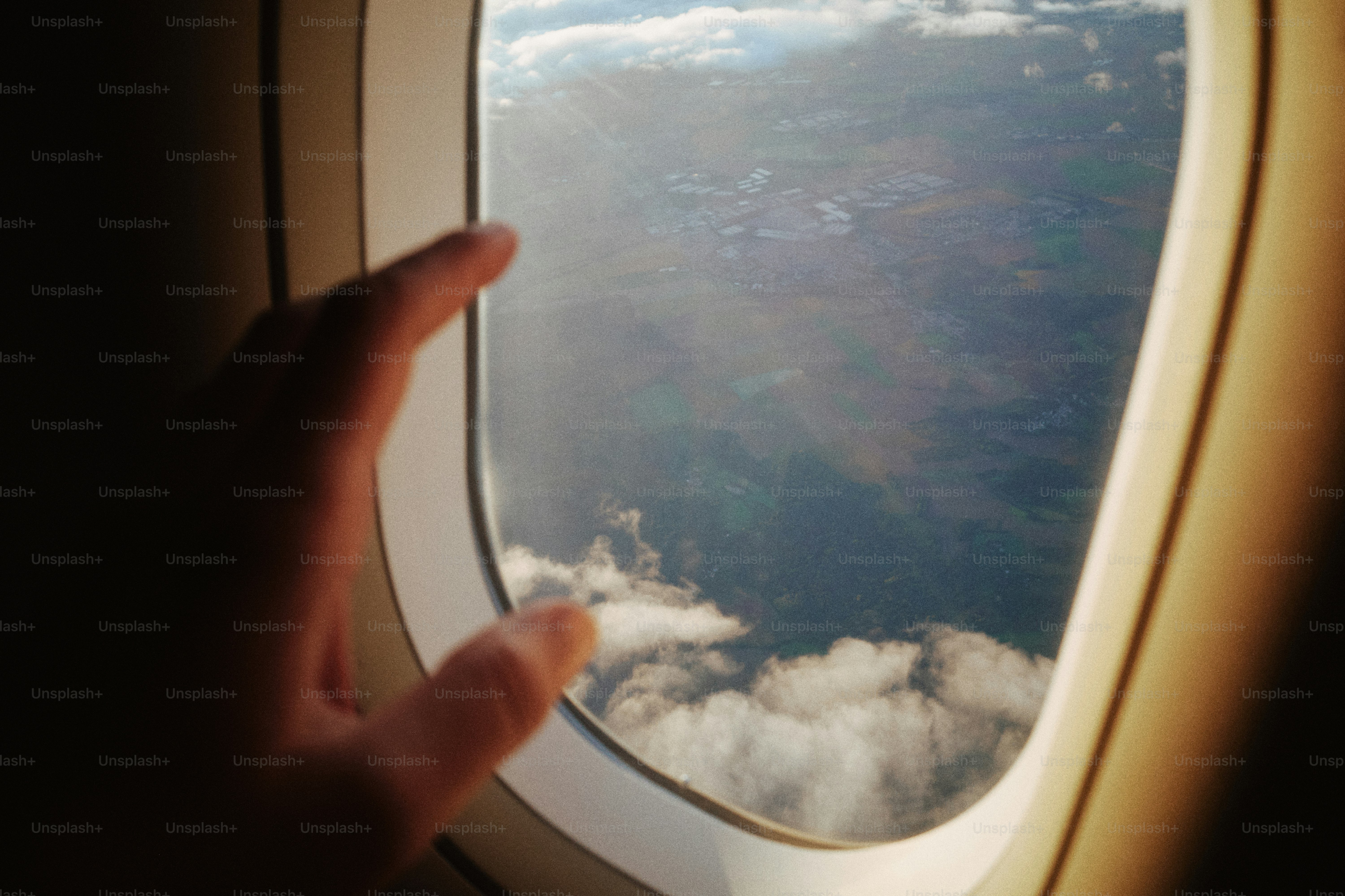 Mano tocando la ventana del avión con nubes debajo.