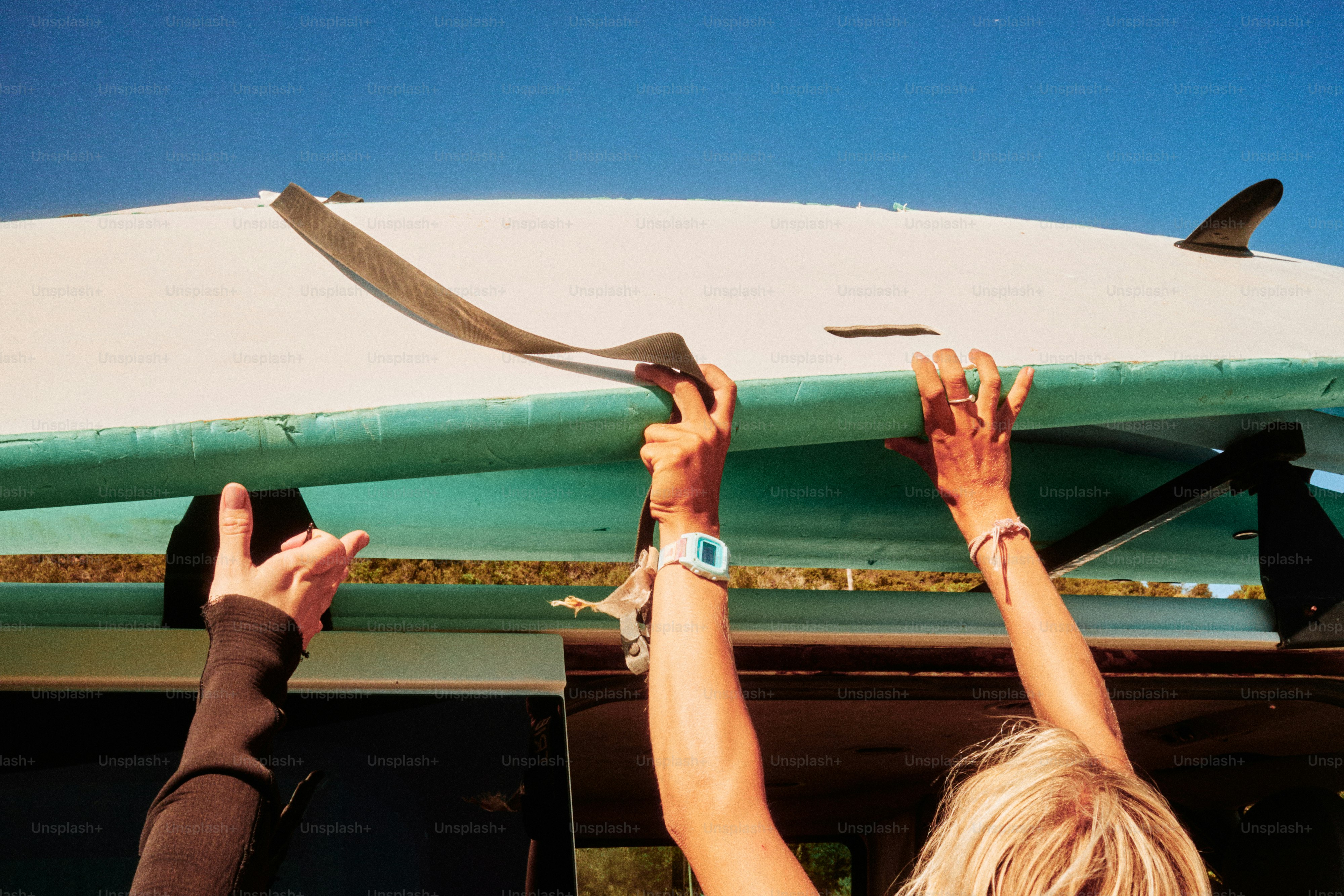 Mani che fissano la tavola da surf al portapacchi del tetto dell'auto