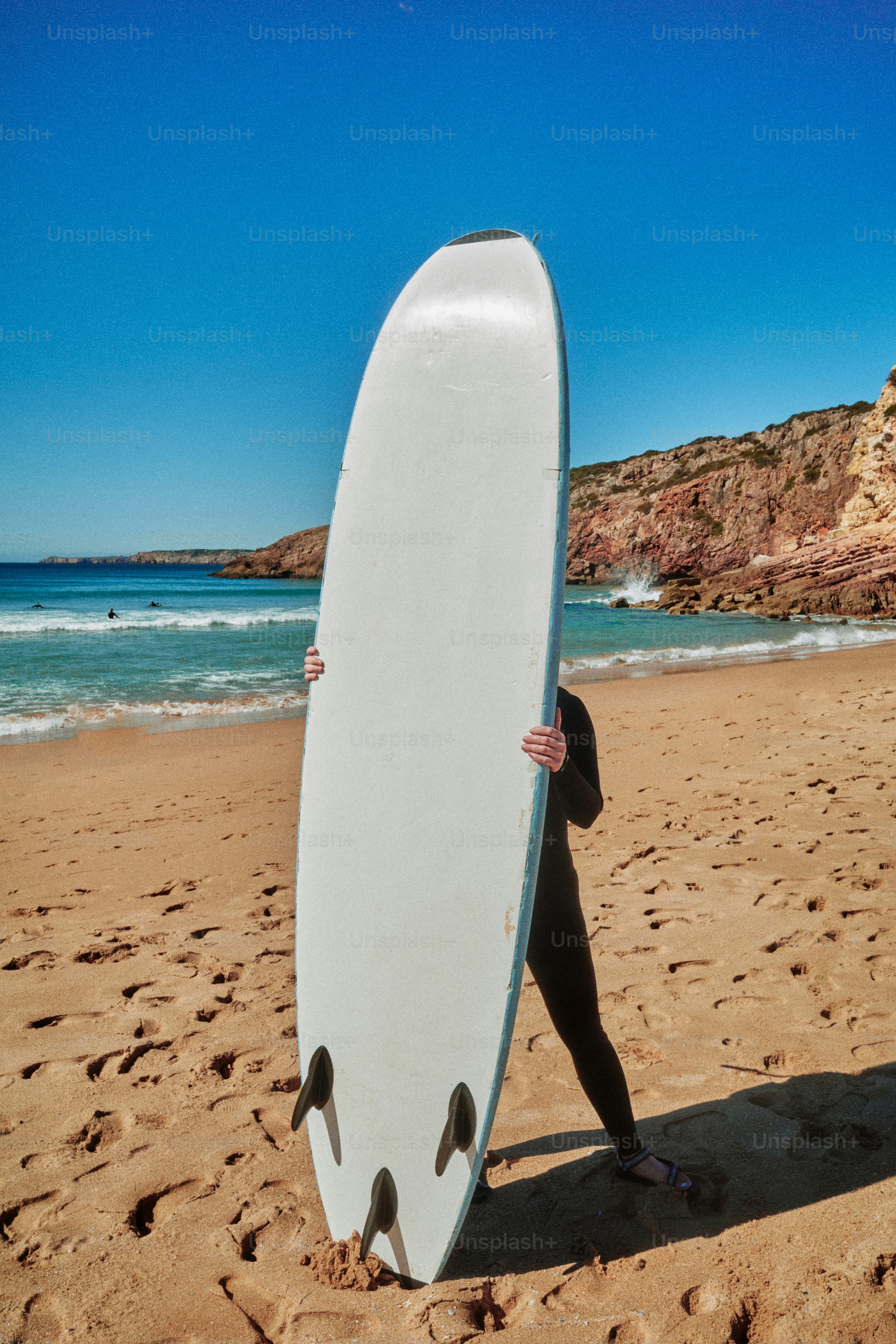 Persona con traje de neopreno sujetando una tabla de surf en la playa
