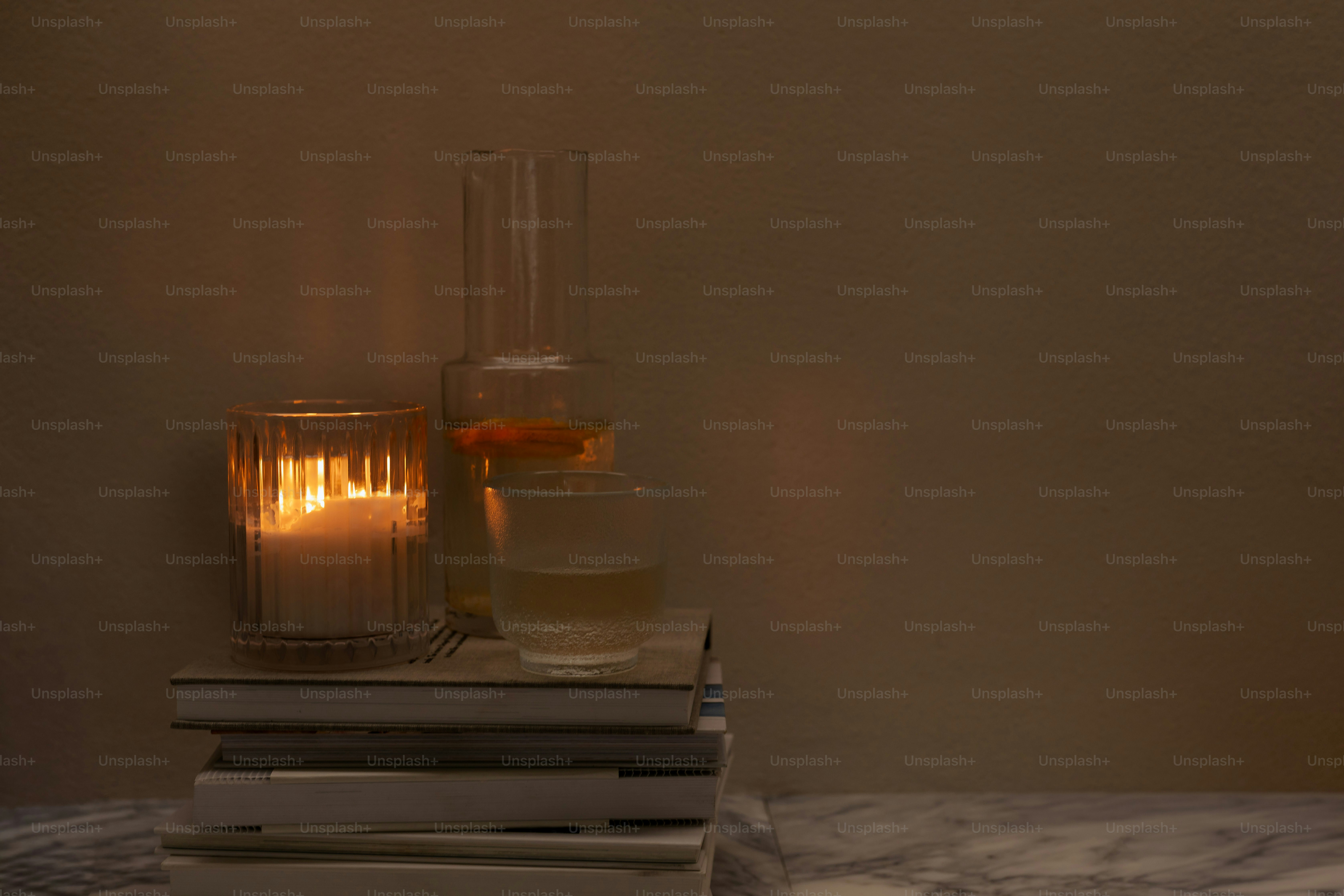 Candle lit beside books and glass bottle