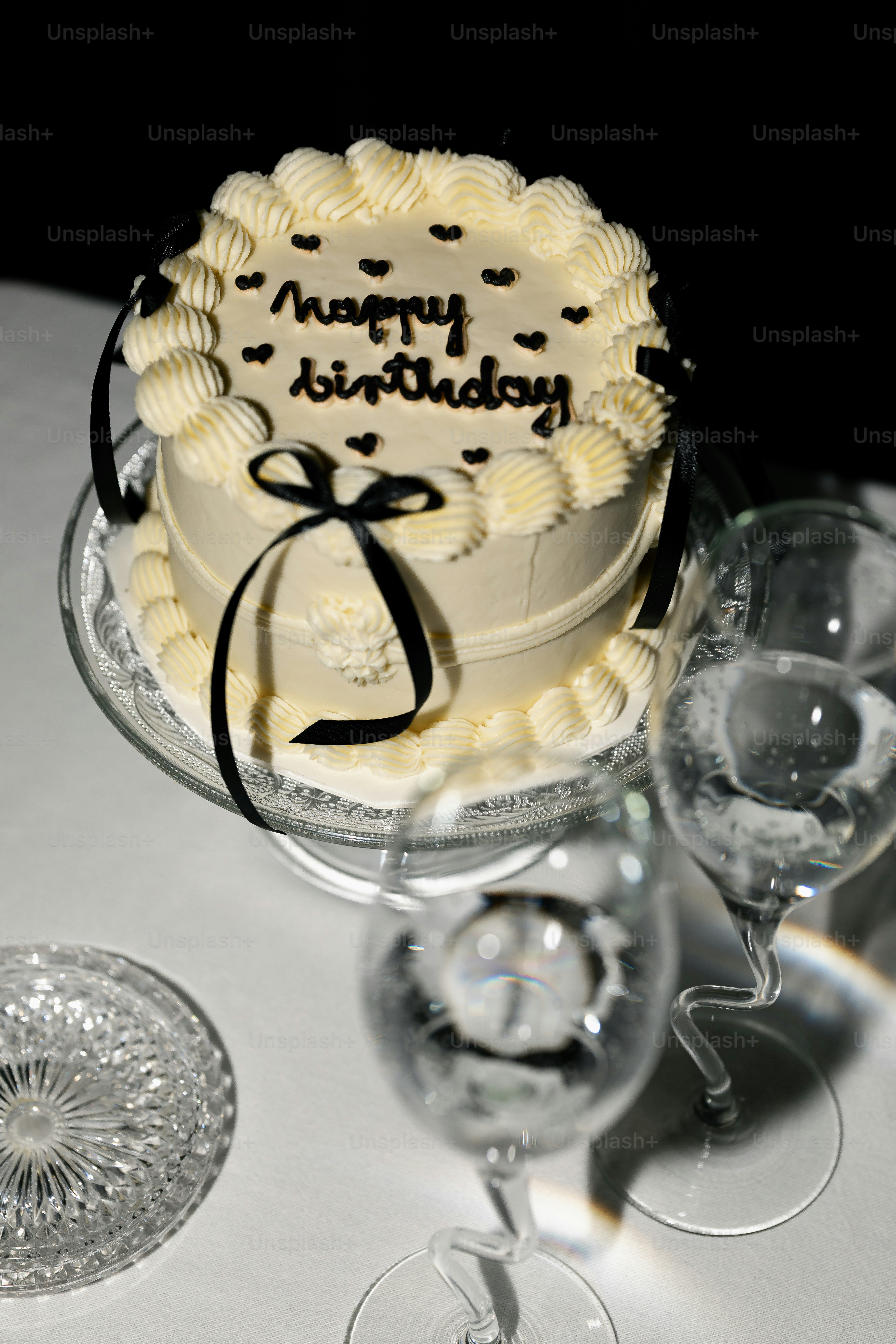 A white birthday cake with black ribbon and white decorations